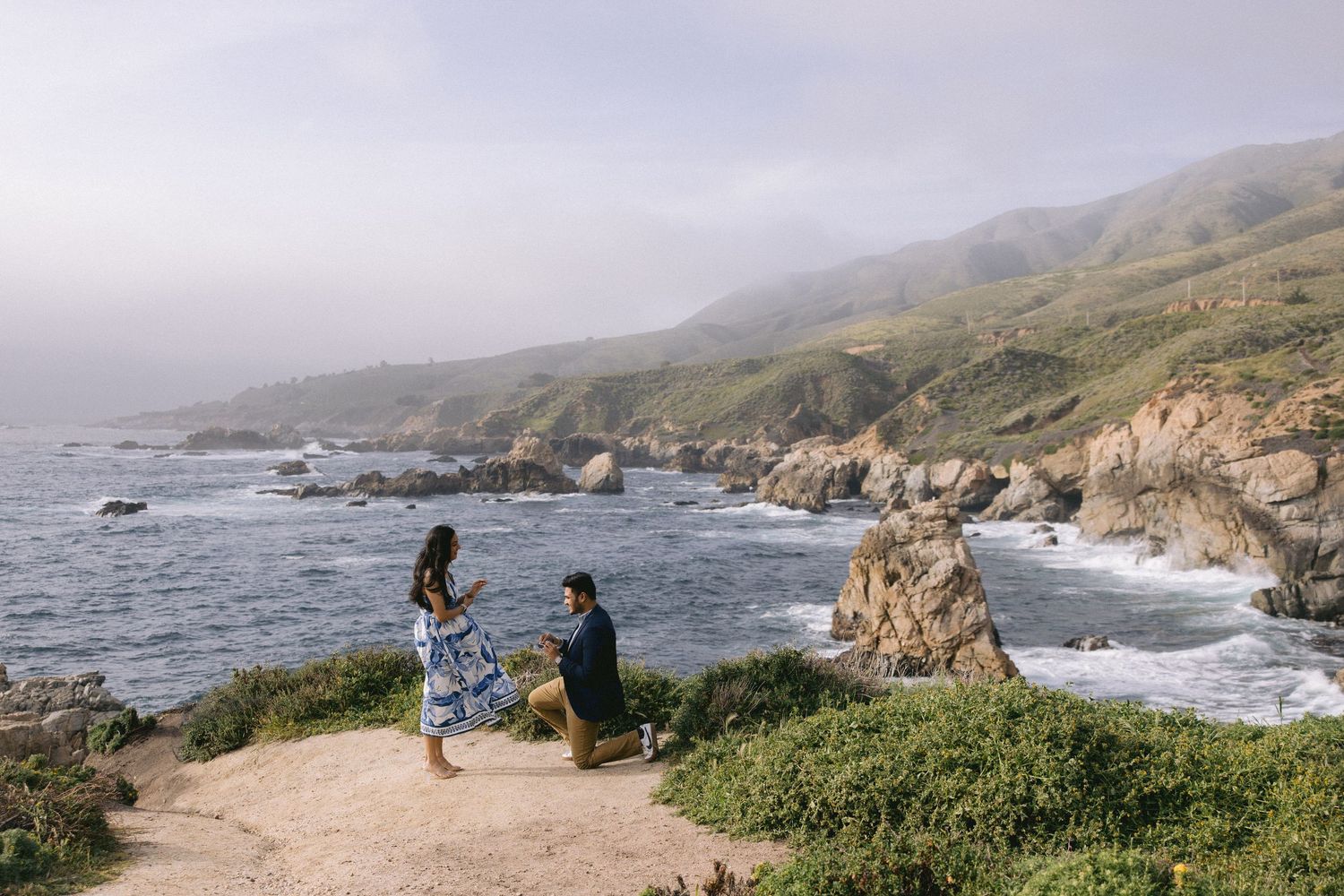 Two people enjoying scenic views of the rugged Big Sur coastline with crashing waves and cliffs in California.