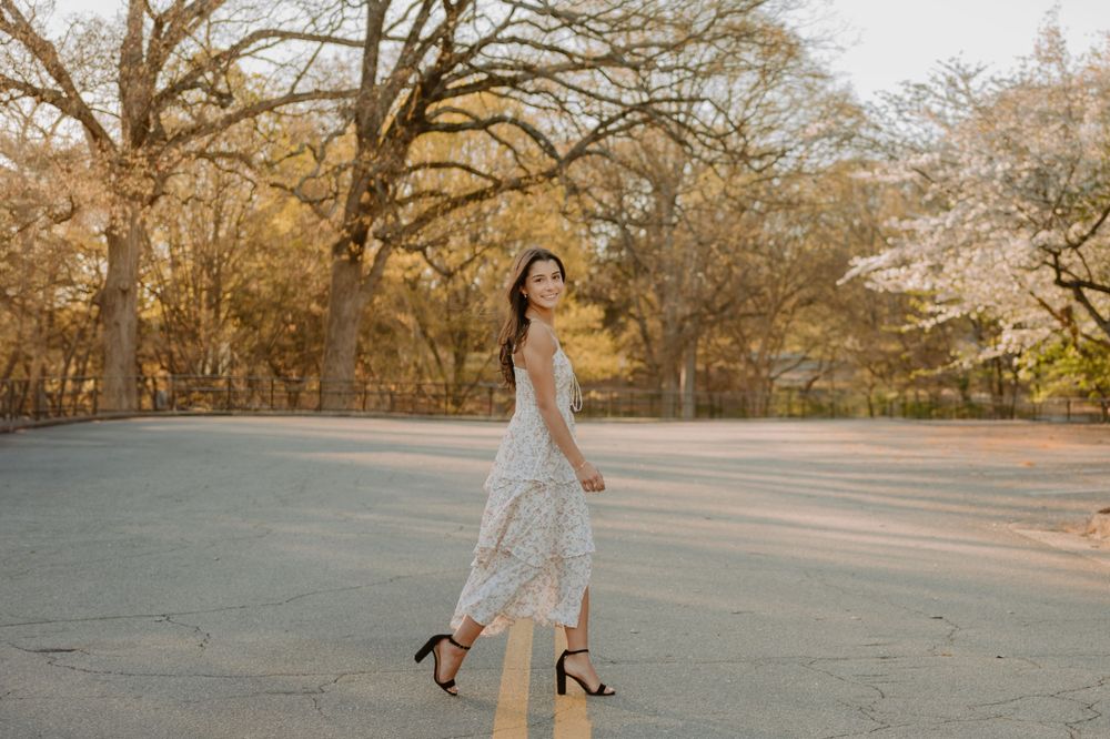 A graceful figure in a lace dress twirls on a pathway surrounded by autumn trees.
