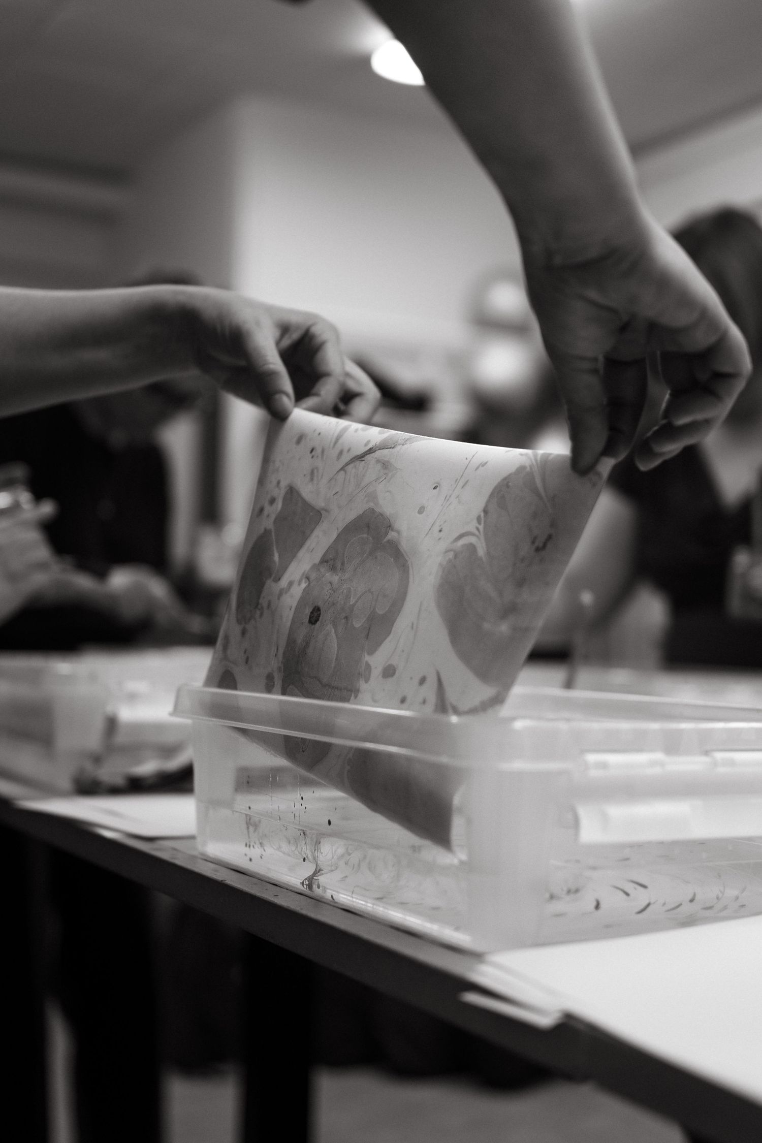 detail on woman's hands pulling out a marbled paper from a container during workshop in Stockholm while being captured by event photographer