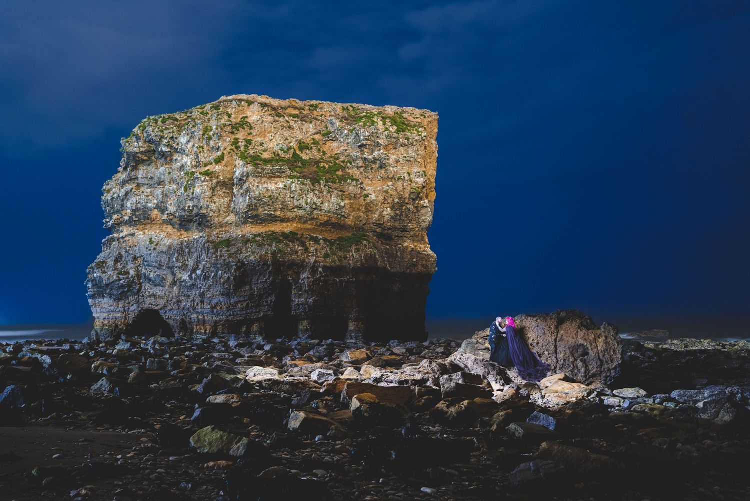 A dramatic nighttime photo of a rock formation with figures in the foreground.