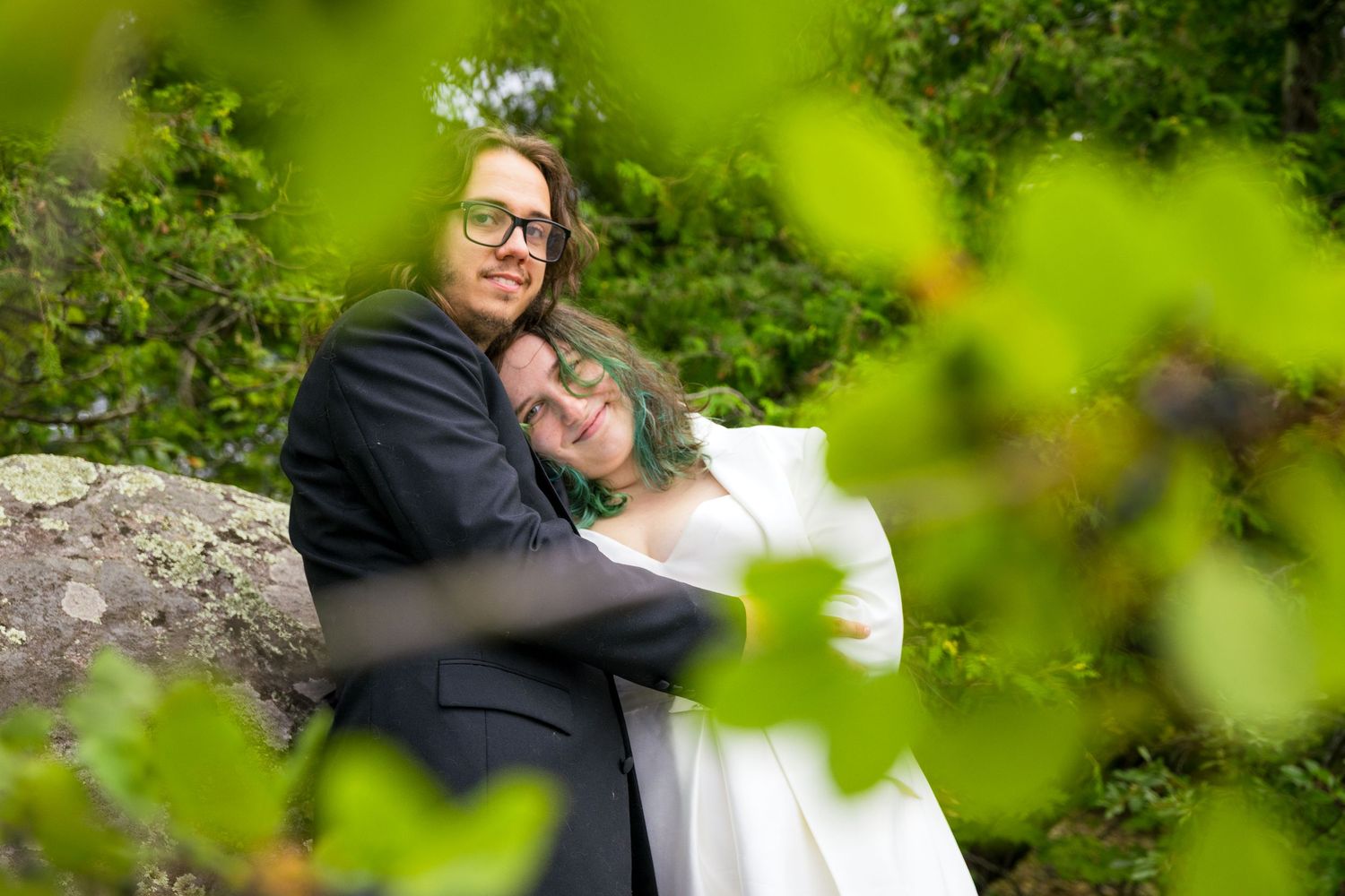 Wedding couple embracing among green foliage with soft focus effect.