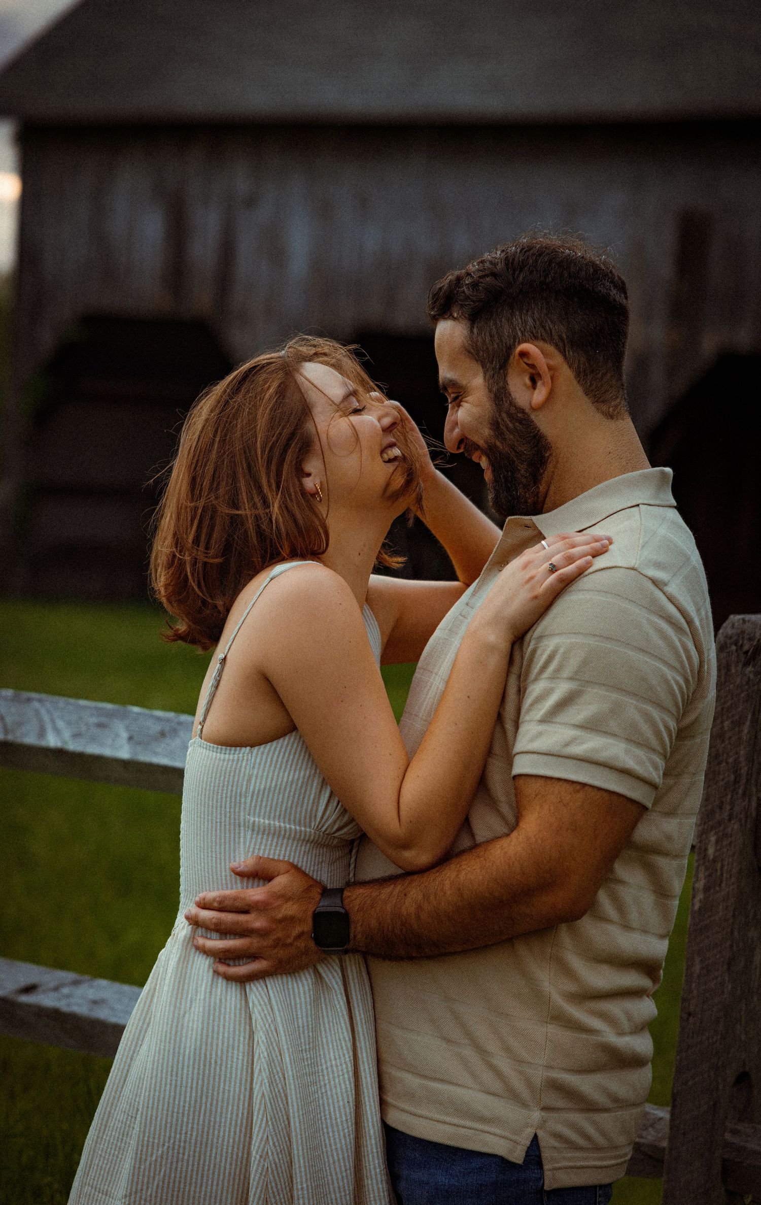 Romantic couple sharing an intimate moment while embracing by a wooden fence at sunset.