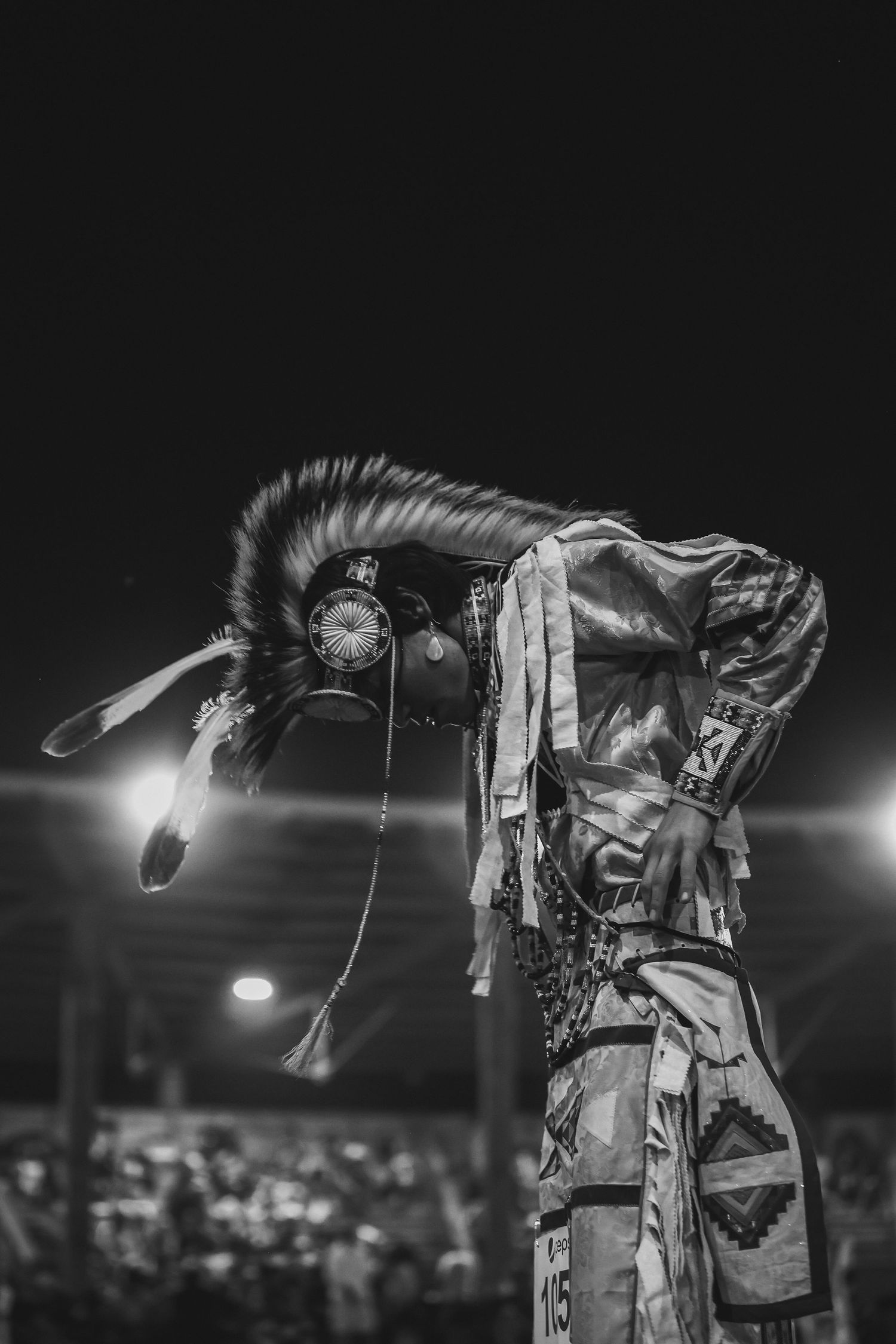 Black and white image of a Native American dancer in traditional regalia performing at night.