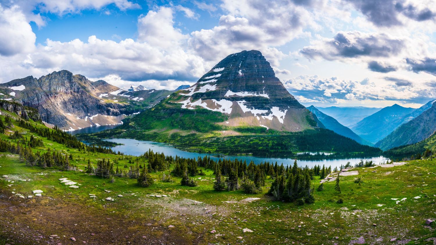 Hiker overlooking majestic mountain peaks with beargrass flowers in the foreground.