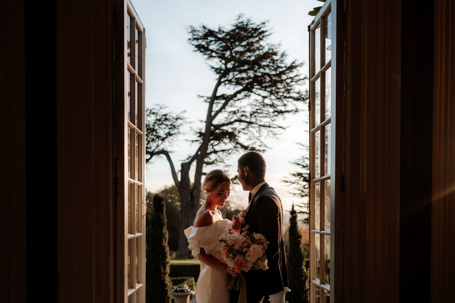 A couple stand together in a doorway at Hedsor House in sunset light on their wedding day. Planning an introvert friendly wedding.