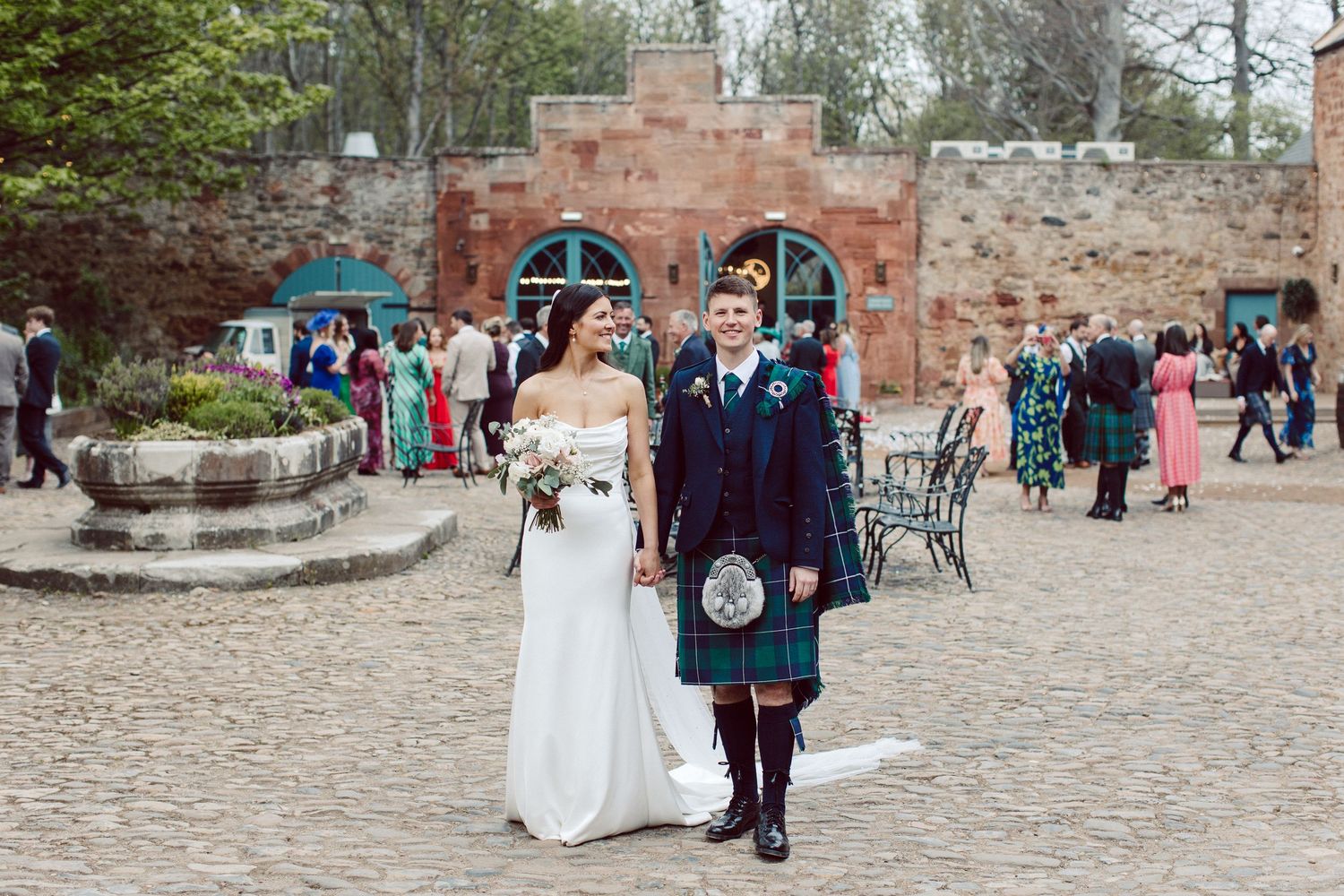 Couple walking along a stone path through a garden setting on their wedding day.
