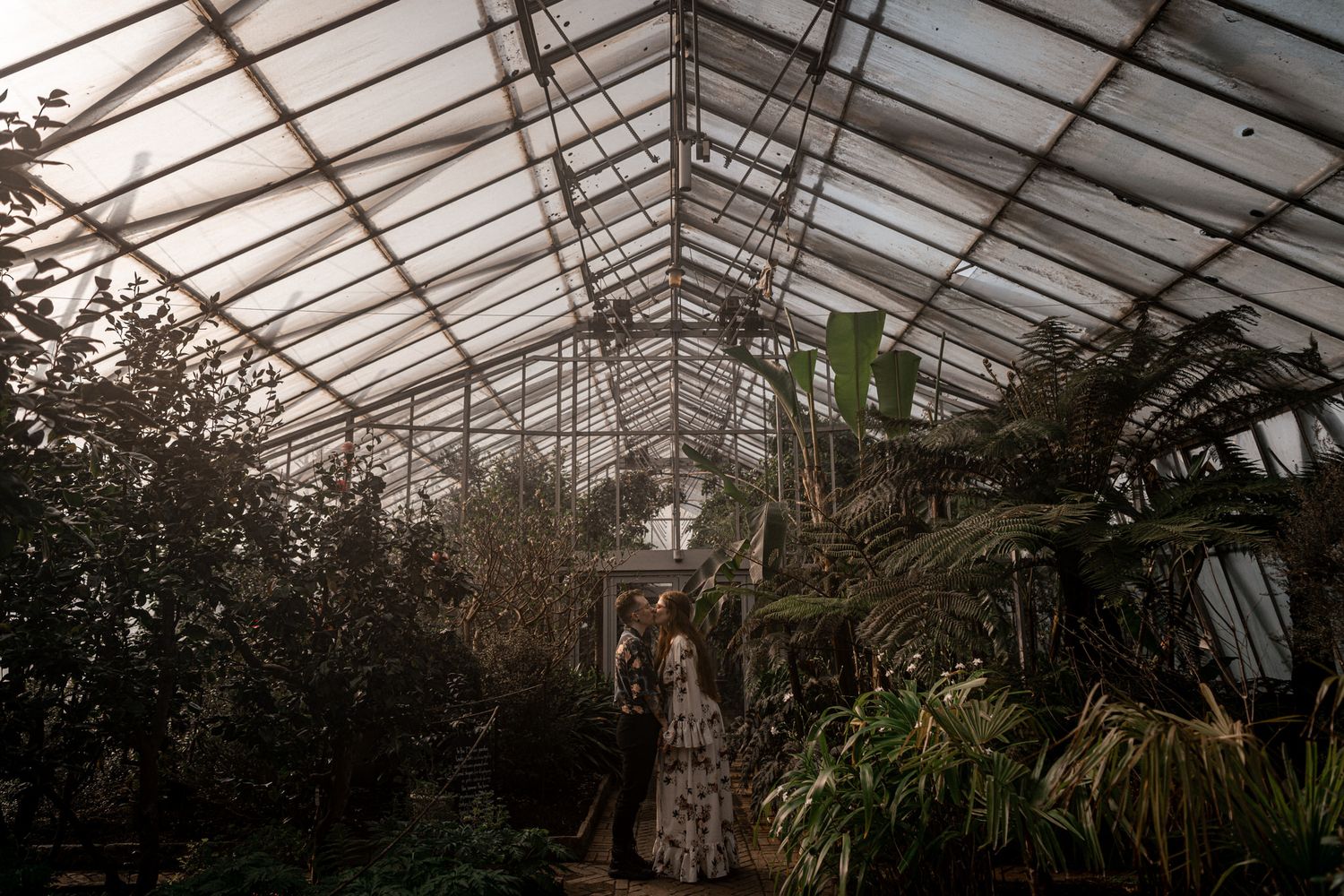 Interior view of a large greenhouse with glass ceiling and tropical plants growing inside.
