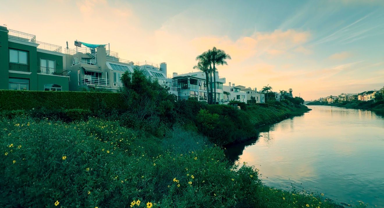 A panoramic sunset view of a coastal town with palm trees and buildings overlooking a tranquil waterway.
