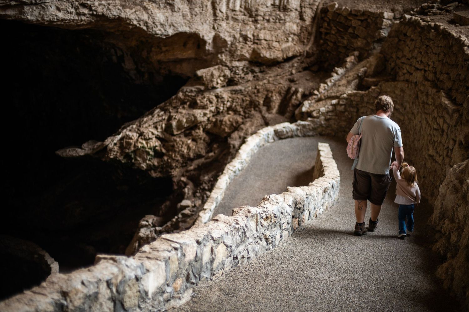 Adult and child walking along a stone path inside Carlsbad Caverns National Park cave tunnel.