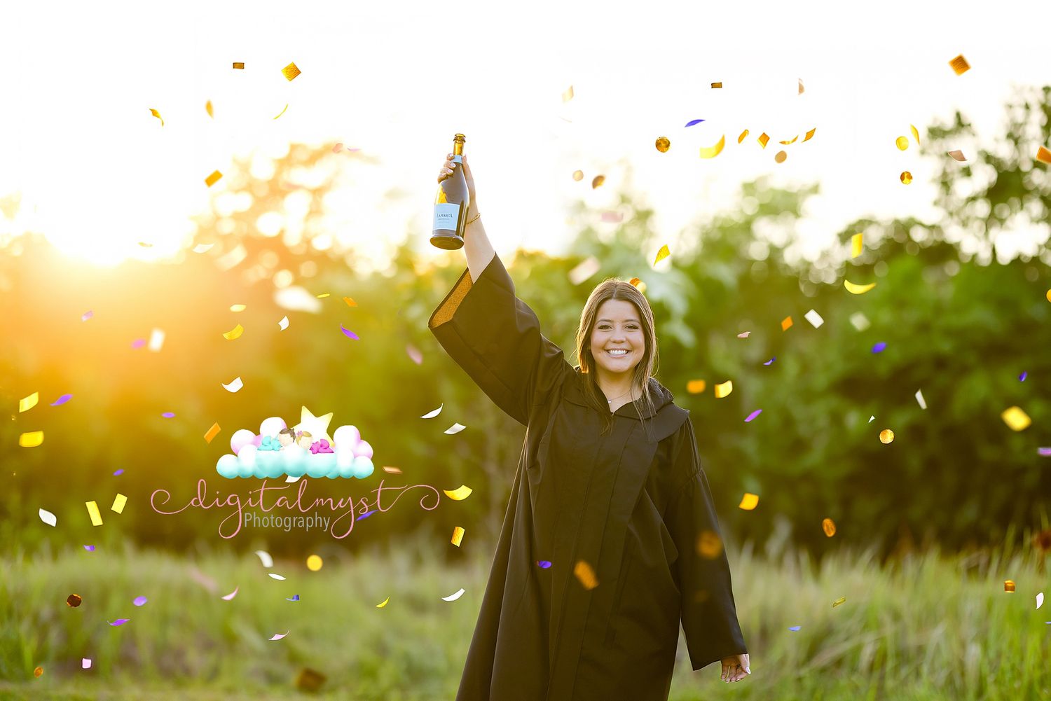 Smiling graduate in black cap and gown celebrates outdoors with confetti and raised bottle at golden sunset.