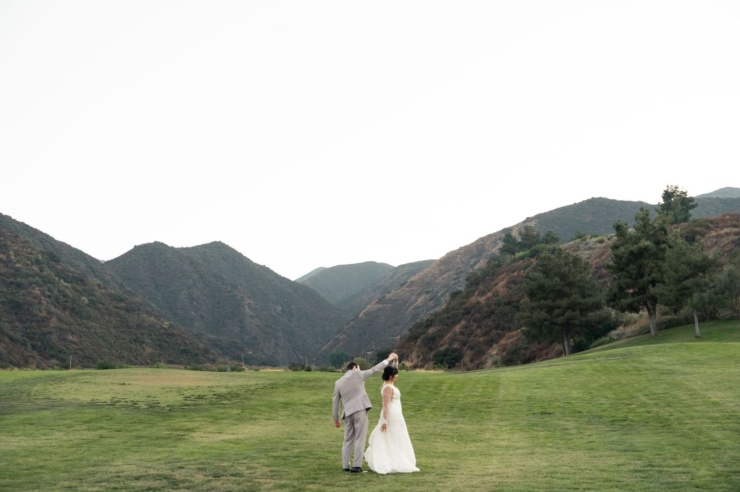 Bride and groom walk down white aisle after outdoor garden wedding ceremony under white pergola.