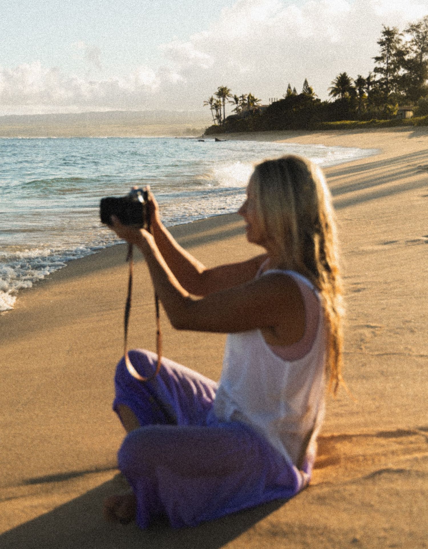 Photographer capturing ocean views at sunset on a North Shore Oahu beach surrounded by palm trees.
