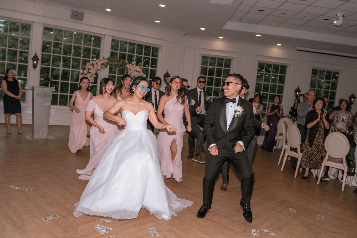 Bride and groom share a joyful first dance surrounded by bridesmaids in pink dresses at an elegant wedding reception.