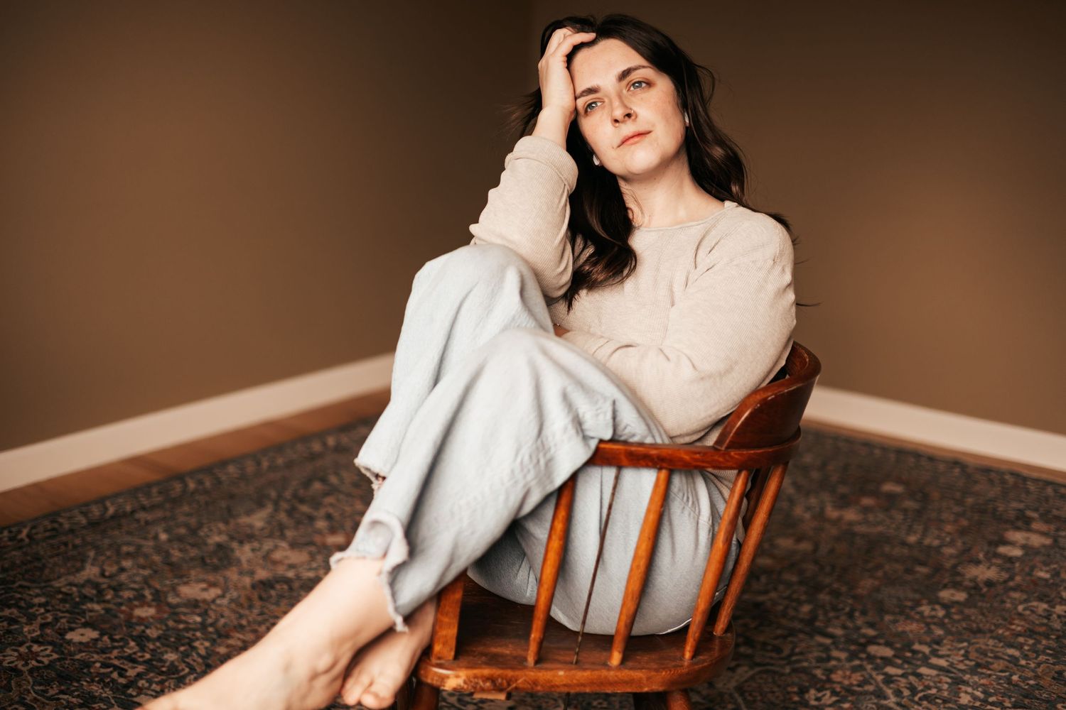 Woman in casual attire sitting relaxed in a wooden chair on a patterned rug | My Postpartum Depression Story