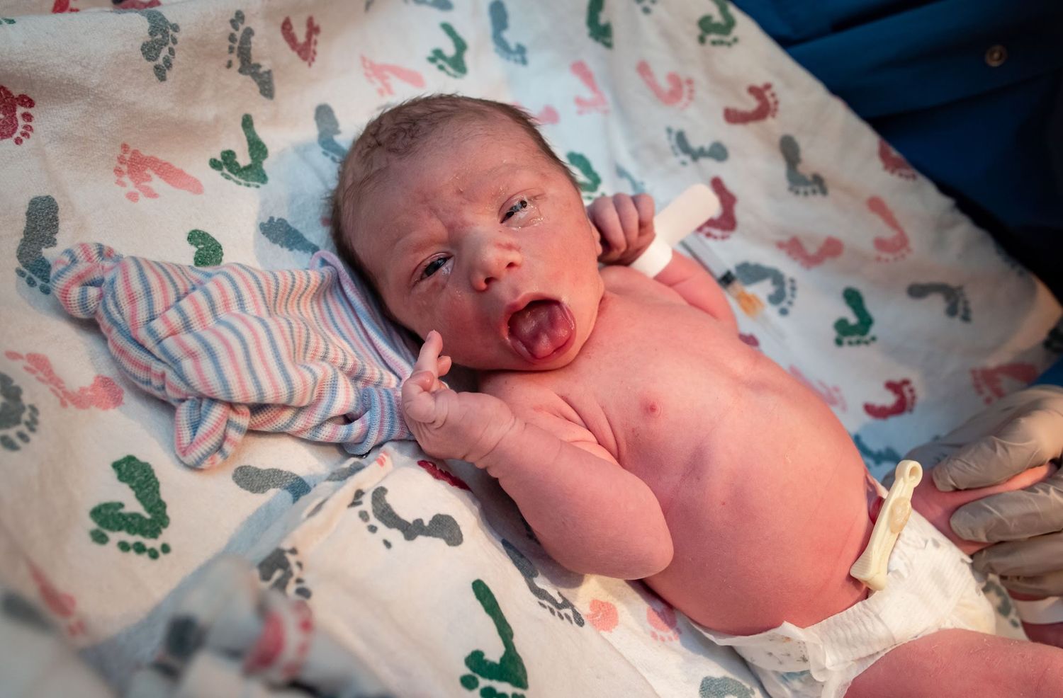 Newborn baby cries while lying on patterned hospital blanket.