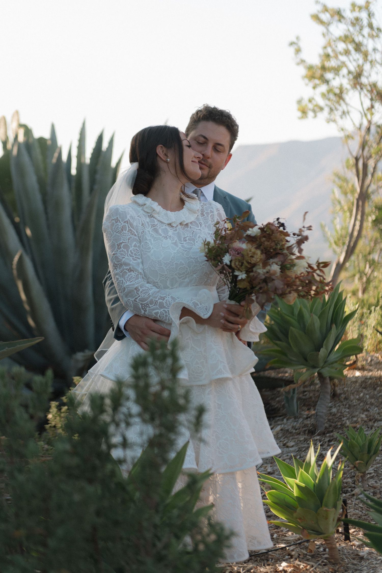 Couple exchanging vows under a white chuppah with mountain views at an outdoor wedding ceremony.