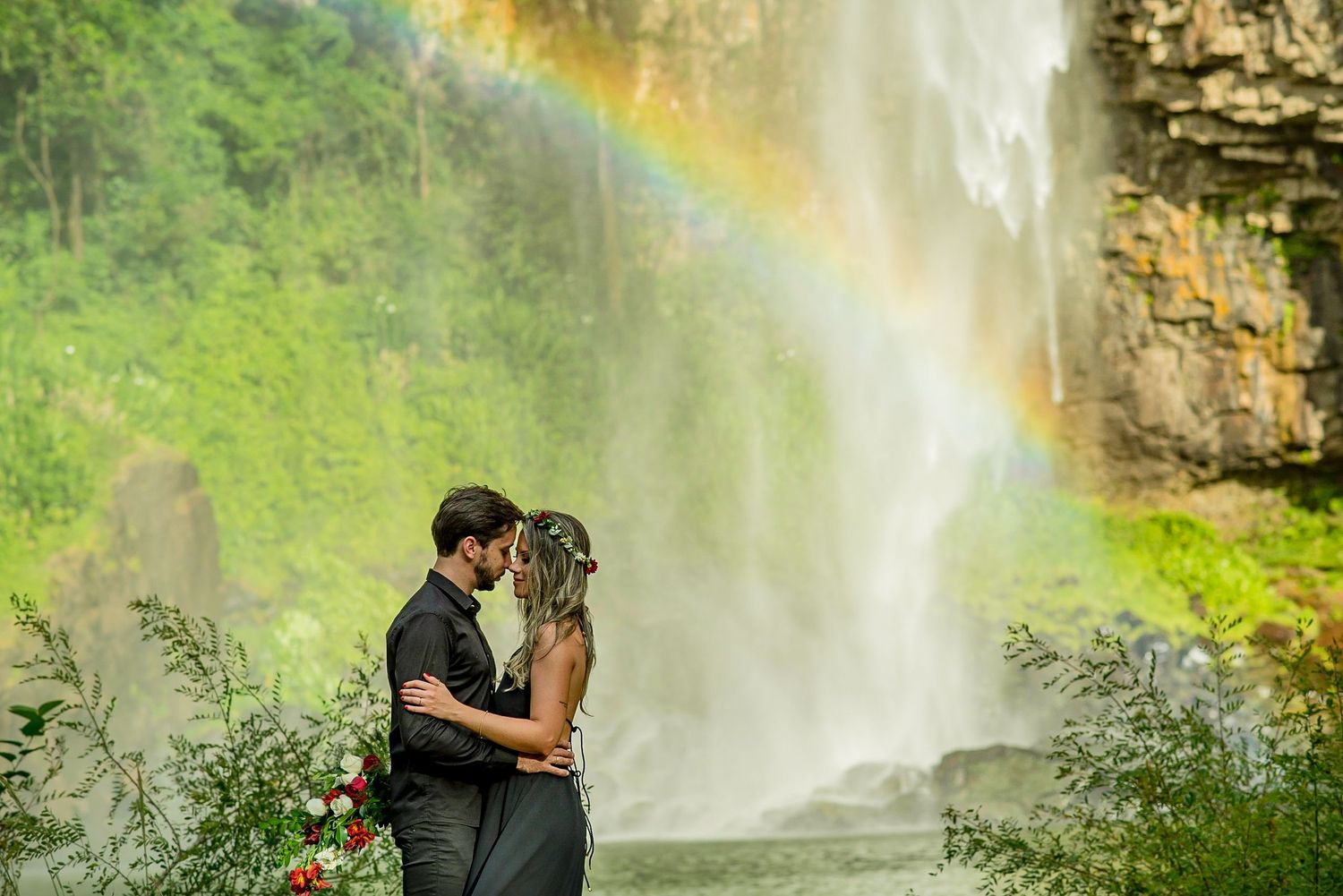 A dreamy waterfall scene with rainbow mist creates magical atmosphere for romantic moment.