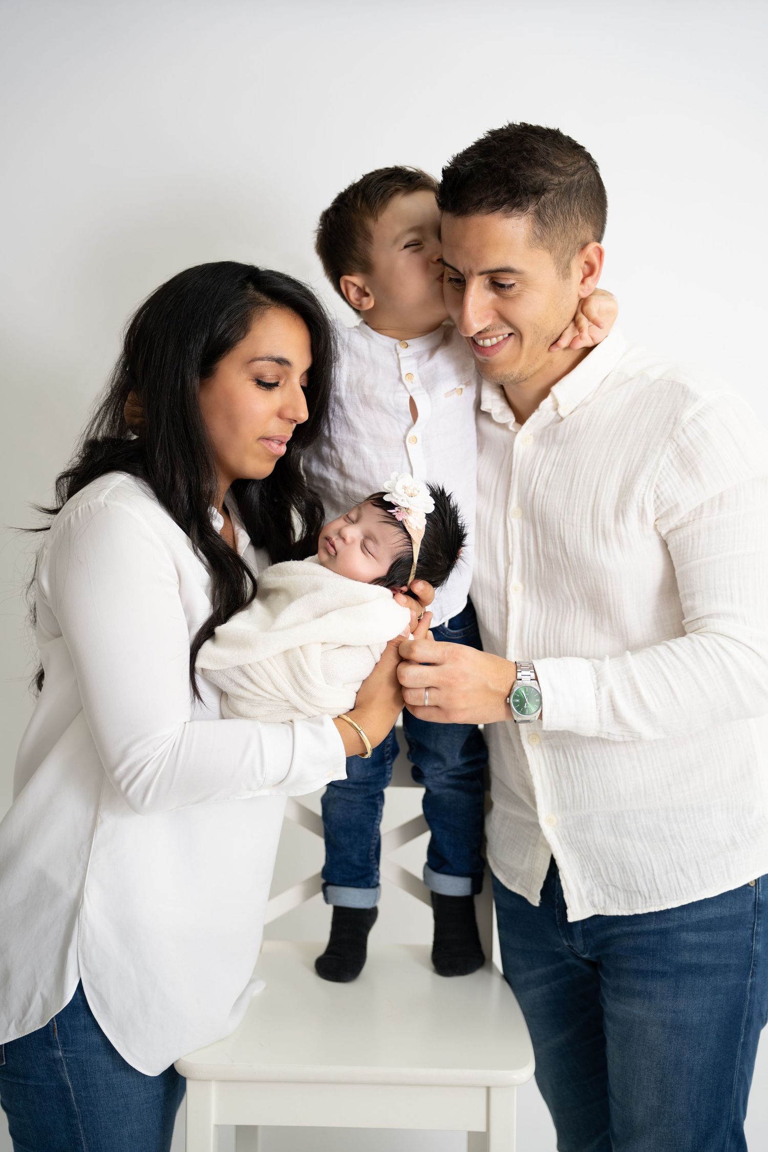 Family wearing white and jeans poses together against white backdrop in studio setting.