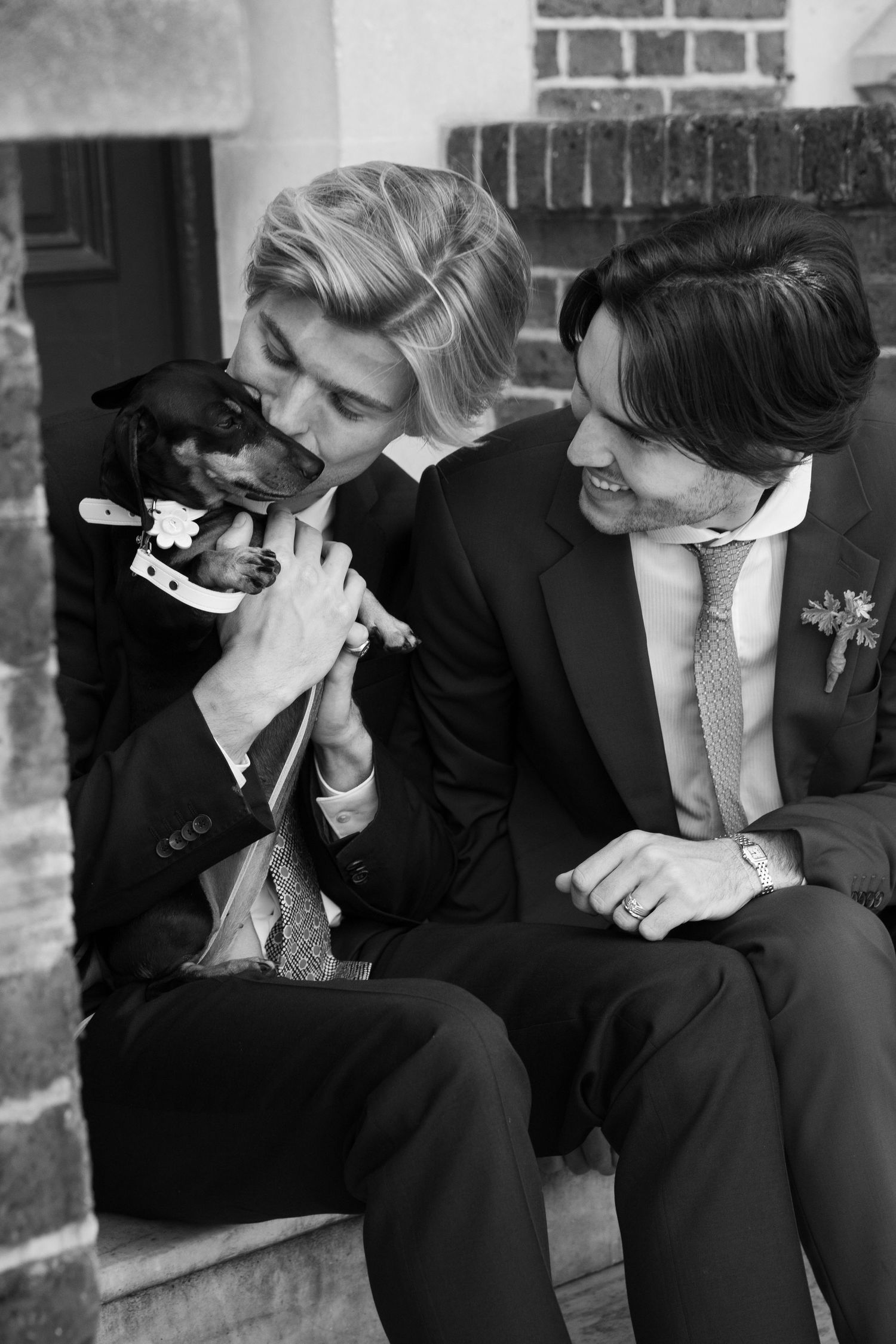 Black and white photo of couple in formal attire sharing a moment with small dog.