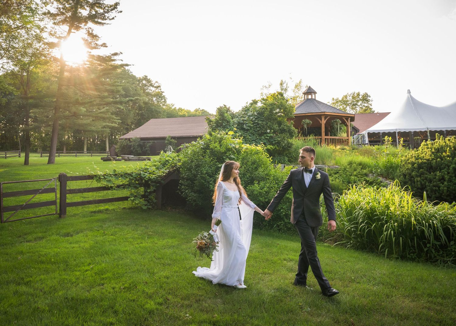 Newlyweds share an intimate moment outdoors with autumn foliage and rustic architecture in background.