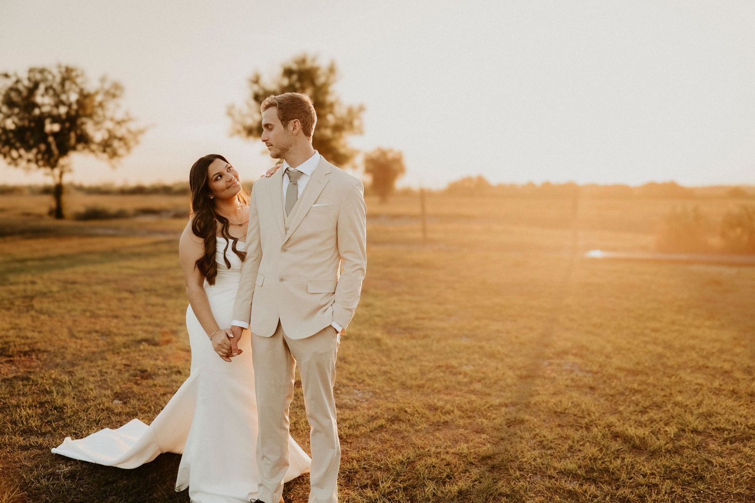A couple shares an intimate moment in a golden sunset field on their wedding day.