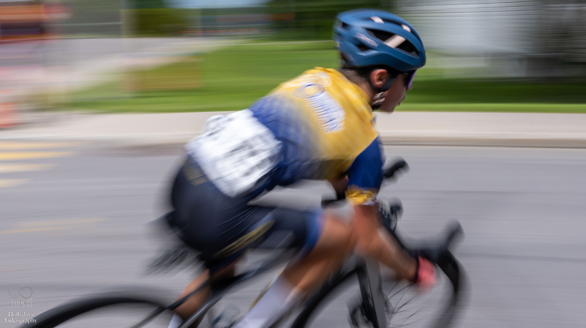 Motion-blurred cyclist in yellow jersey rides racing bike on suburban road during competition or training.