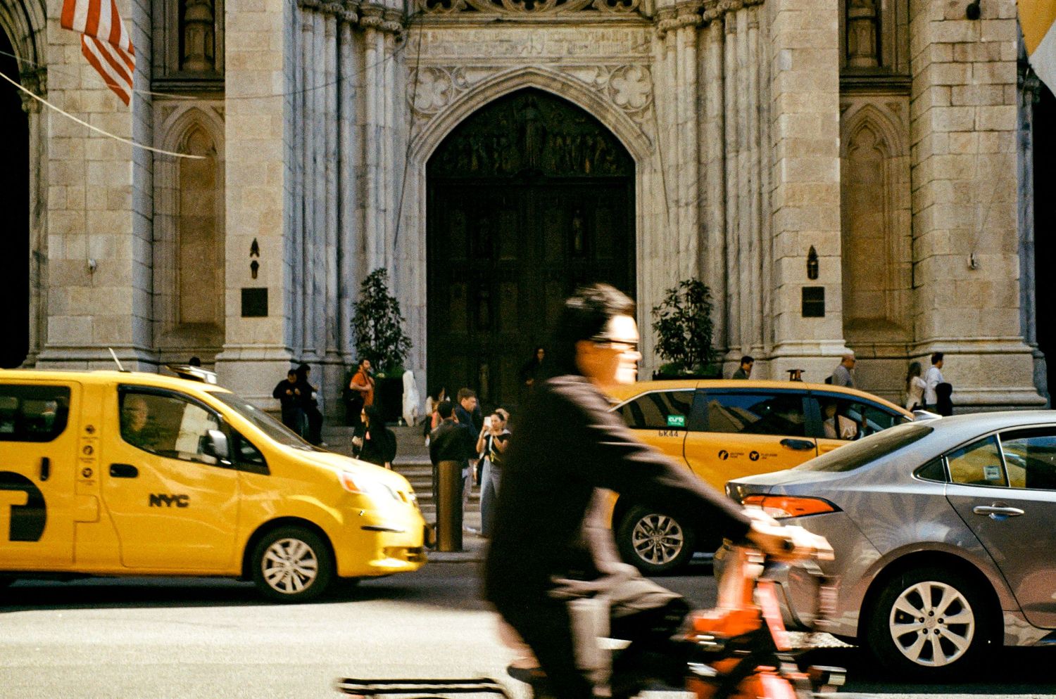 Yellow taxis and cyclists passing by a grand architectural entrance in New York City.