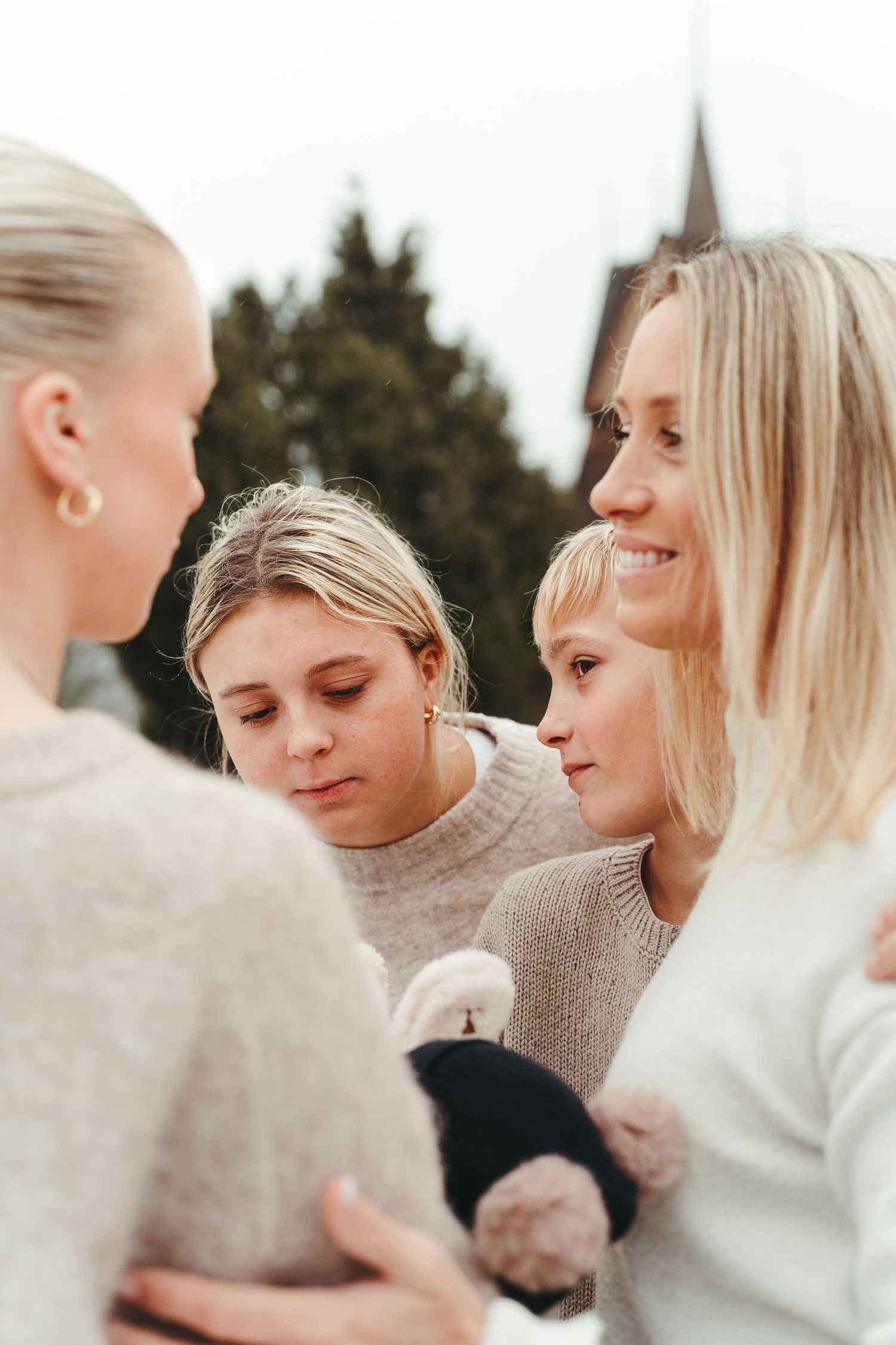 A close group huddles together wearing cozy neutral-colored sweaters in natural light.