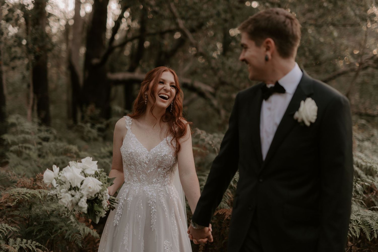 A couple in wedding attire walks together through a wooded outdoor setting during an autumn ceremony. Perth wedding photography
