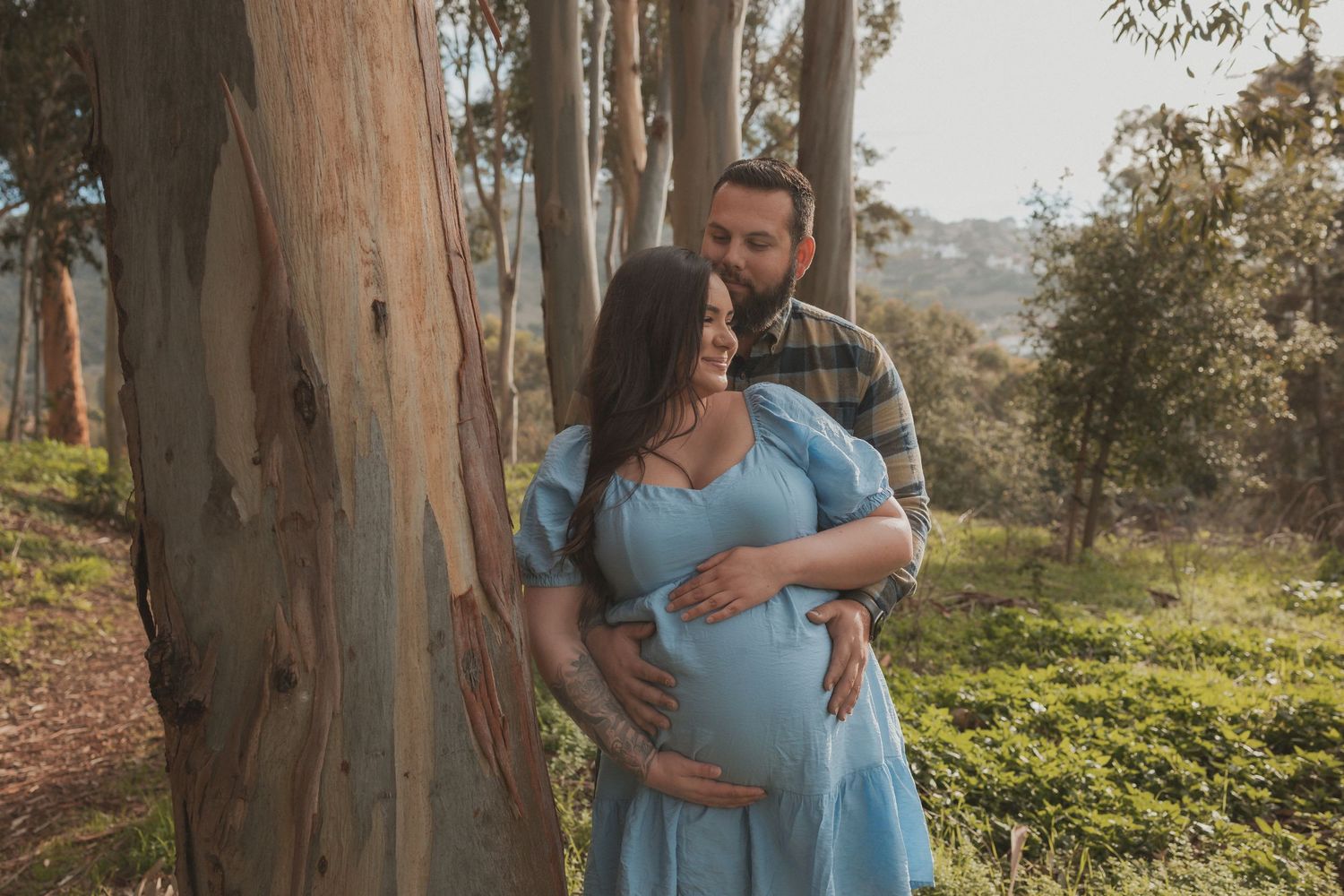 Intimate maternity photo of a couple embracing among eucalyptus trees.