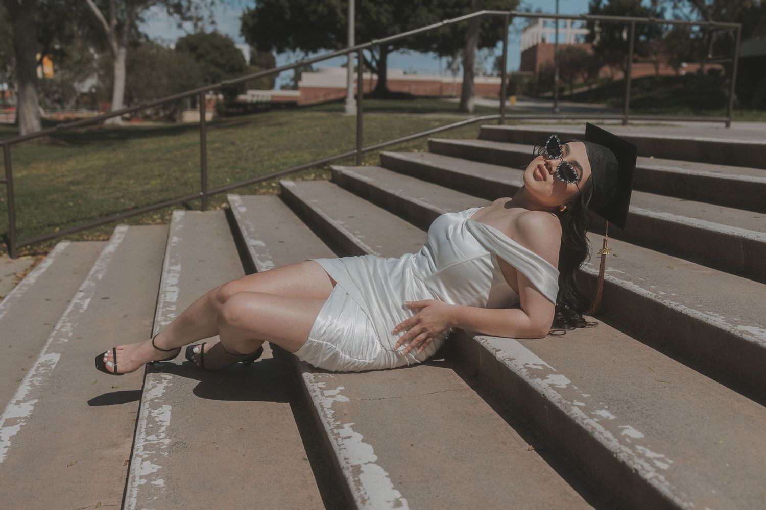 Woman in white dress lounging on concrete steps in sunny outdoor setting.