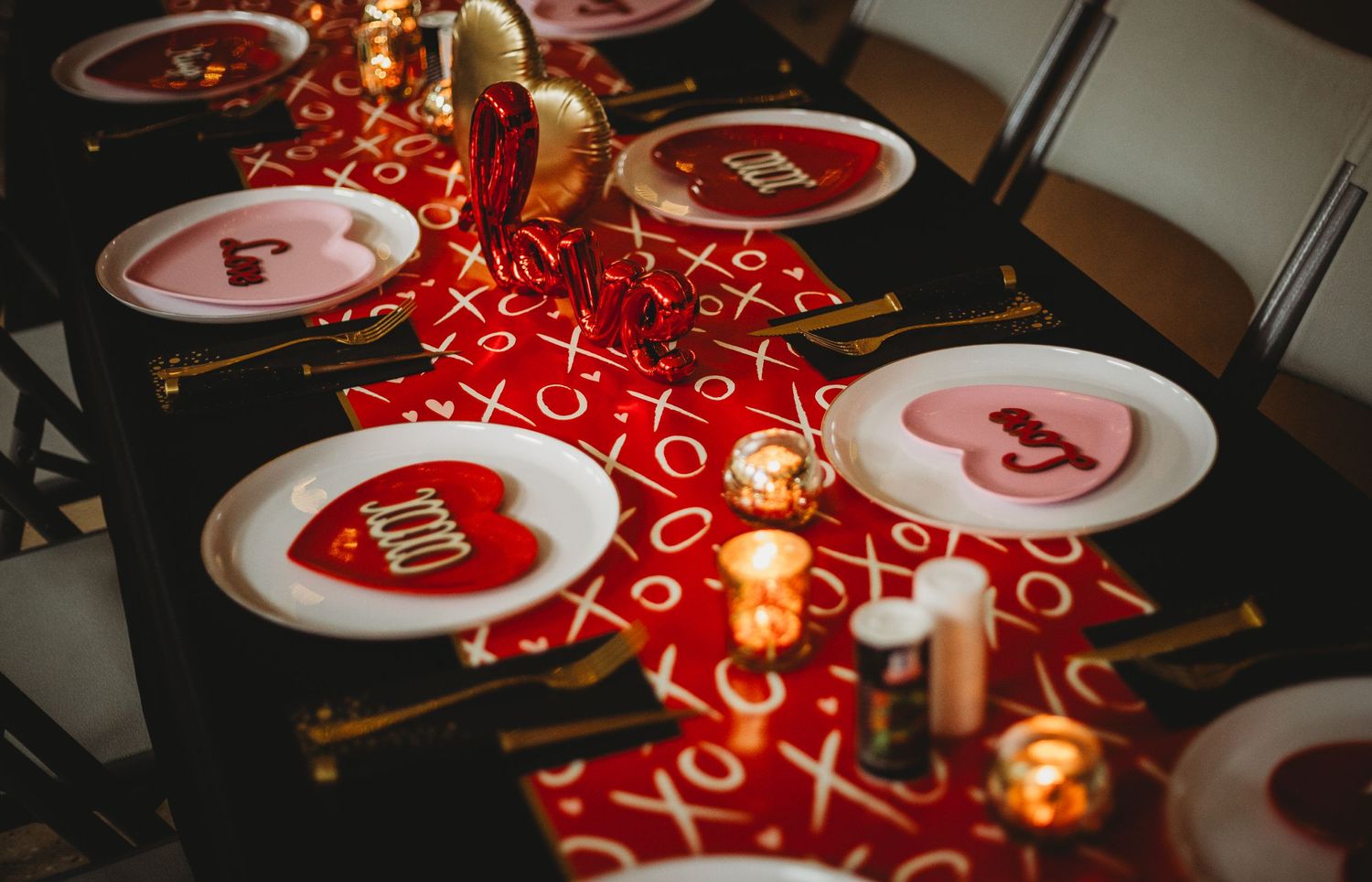 Red Valentine's Day table setting with glowing candles and decorative plates featuring heart designs and XOXO pattern.
