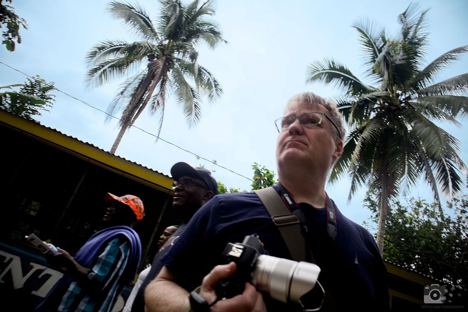 A photographer stands with camera gear under tall palm trees in a tropical setting.