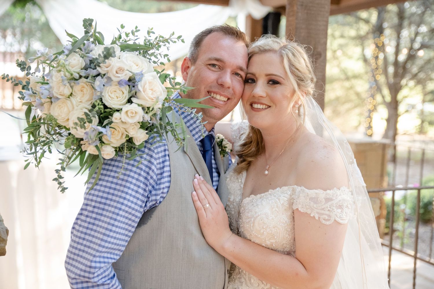 A happy couple at their wedding celebration with a beautiful floral bouquet featuring white and blue flowers in a rustic setting.