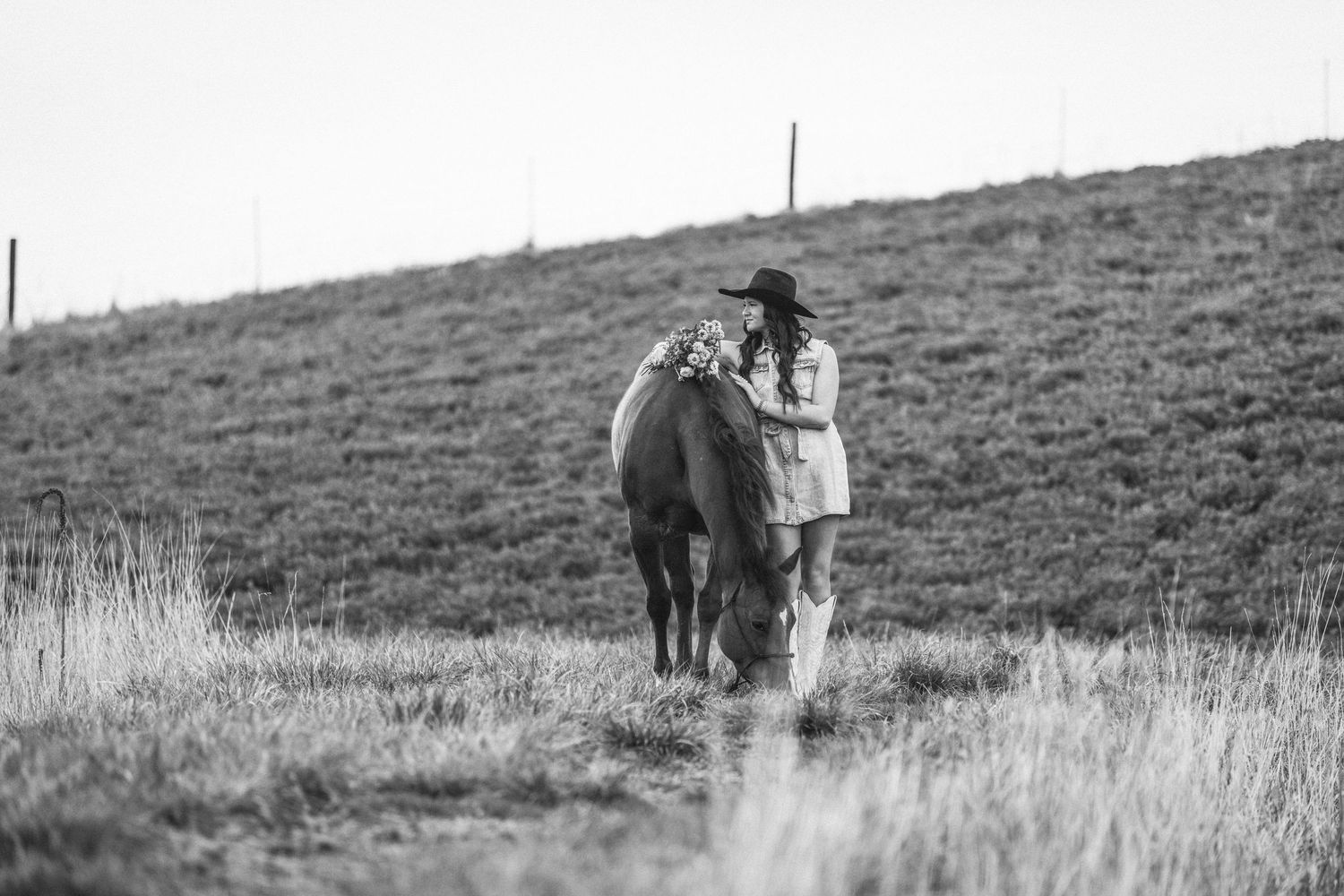 A person in a wide-brimmed hat leads a horse up a grassy hillside slope in black and white.