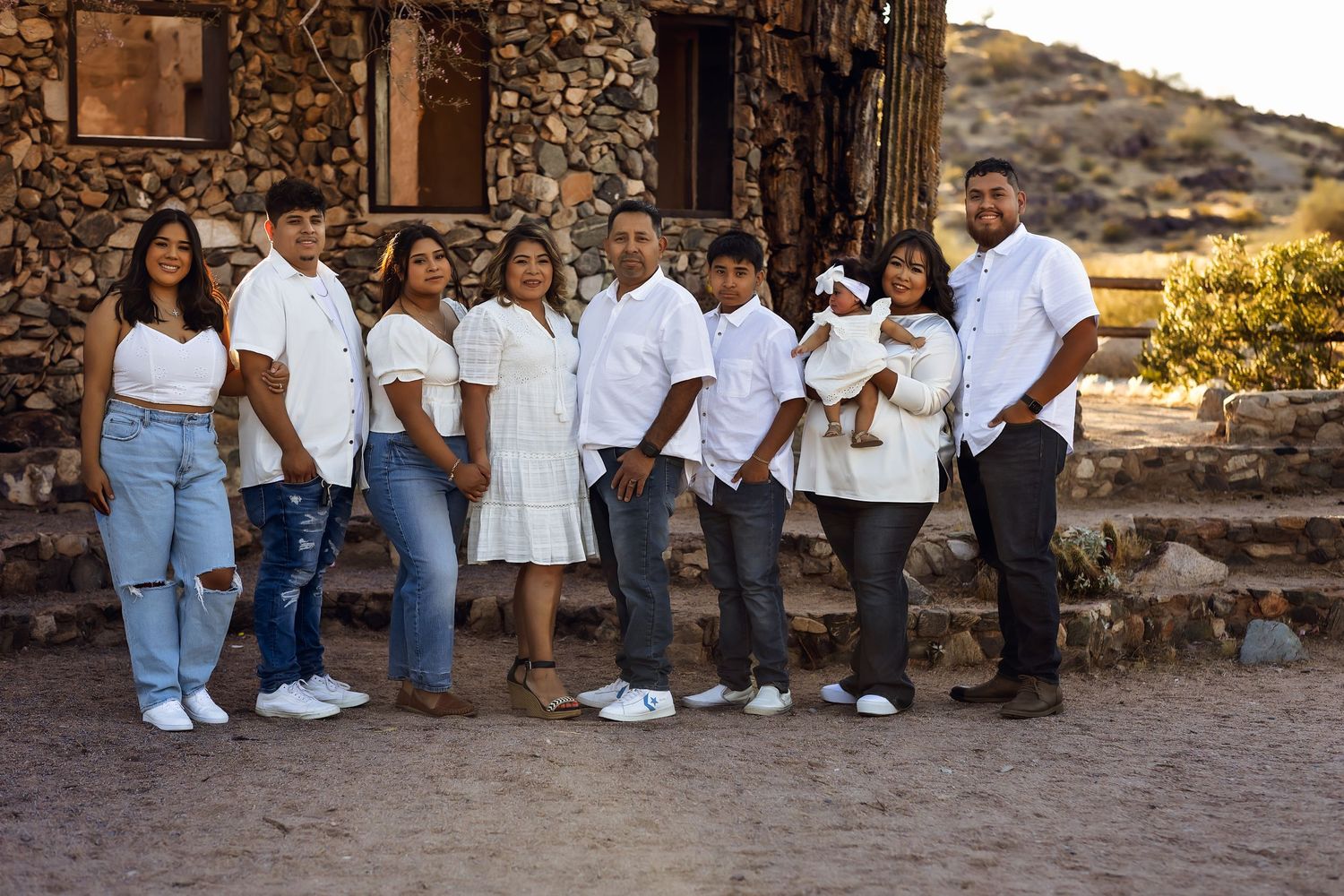 Family photography session with coordinated casual outfits in jeans and white shirts against rustic outdoor backdrop.