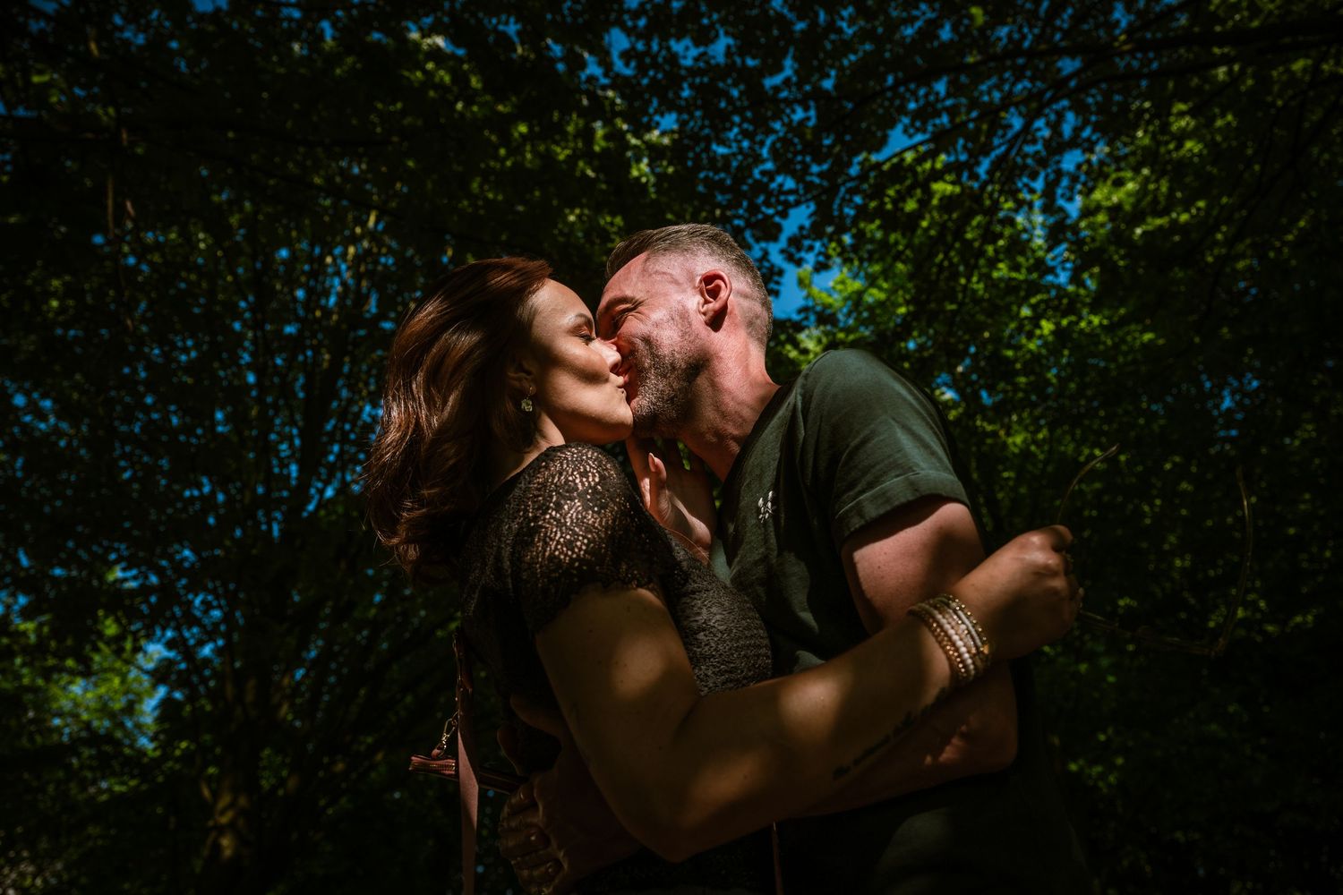 Verloofd koppel in een artistiek beeld bij een gratis pre-weddingshoot van Bart Boodts Photography, de zon schijnt door de bomen.