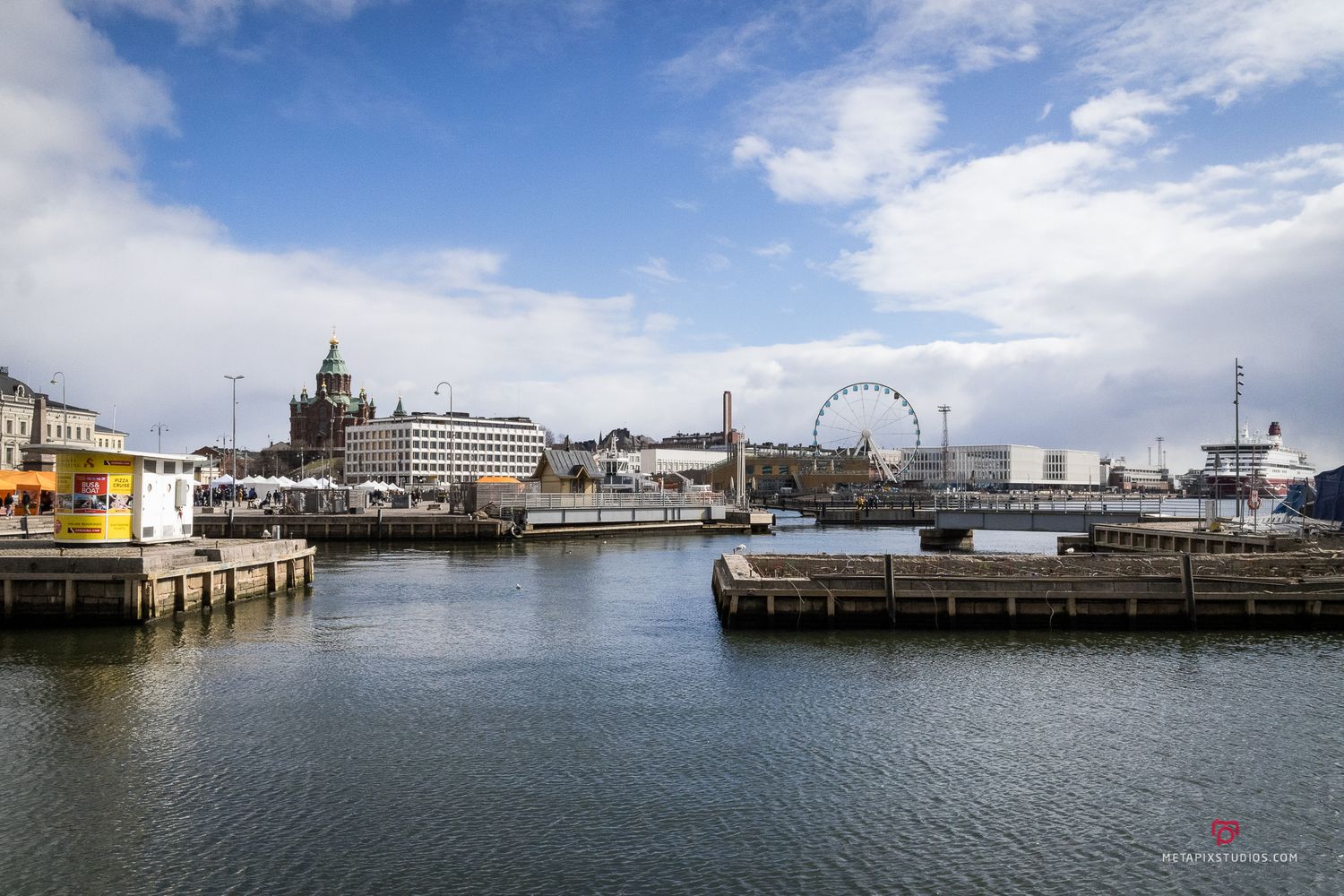 Panoramic view of Helsinki harbor waterfront with Uspenski Cathedral, Ferris wheel, and docked boats on a sunny day.