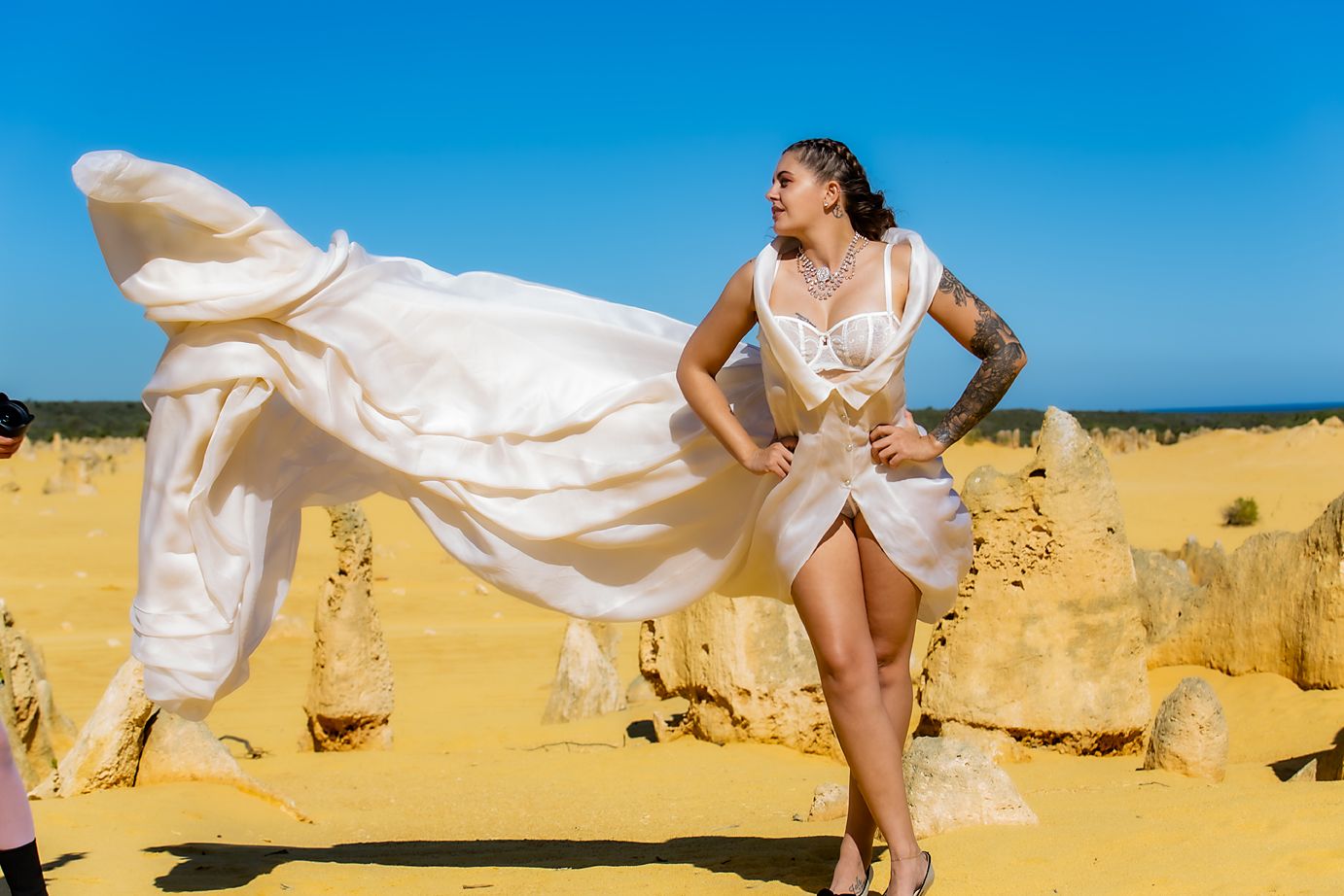 Flowing white veil billows in the wind against sandy desert landscape and bright blue sky.