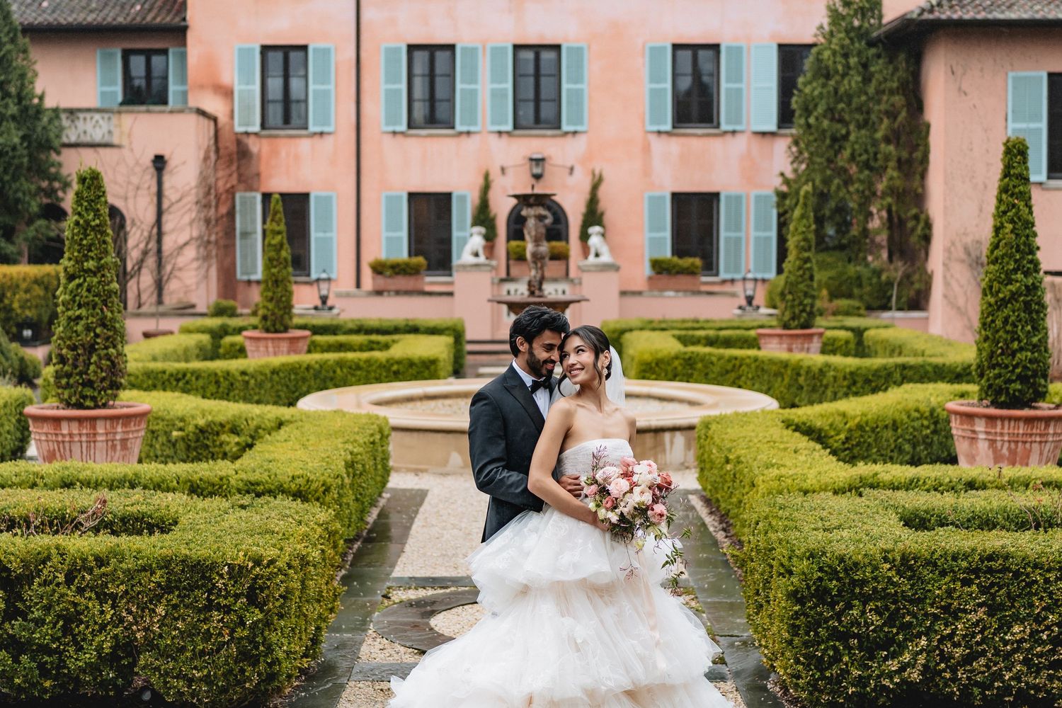 Elegant vintage villa wedding venue featuring manicured hedge gardens and pink-tinted facade in Tuscany.