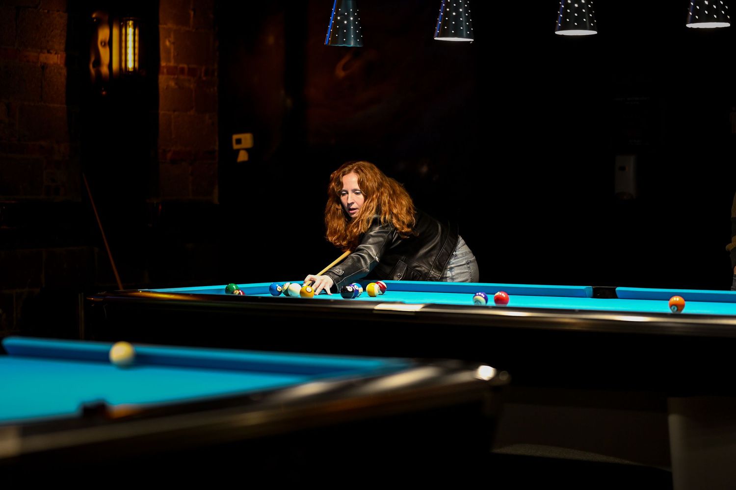 A pool player leans across the billiards table in a dimly lit bar