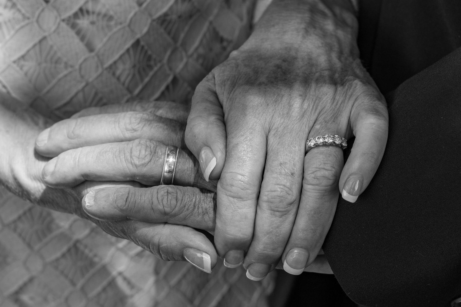 Black and white close-up of hands wearing wedding rings.
