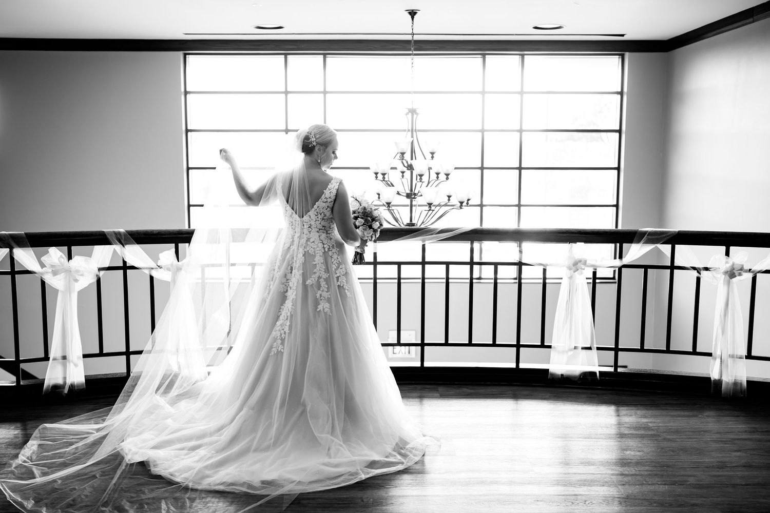 Silhouette of bride in flowing gown near large window with chandelier.