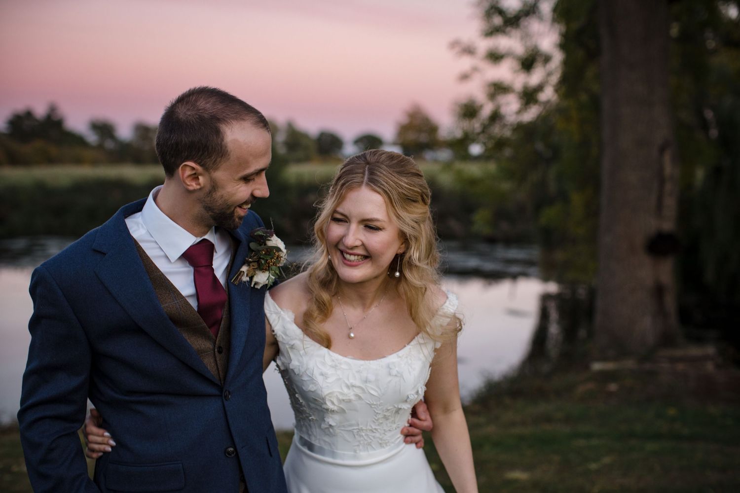 A happy newlywed couple laughs together by a lake during a sunset wedding photograph Saraguay House, Nova Scotia
