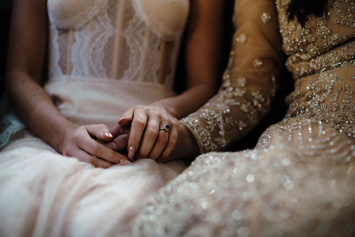Two LGBTQ brides in wedding dresses hold hands together in a tender moment captured in soft lighting at The Lord Nelson Hotel, Halifax.
