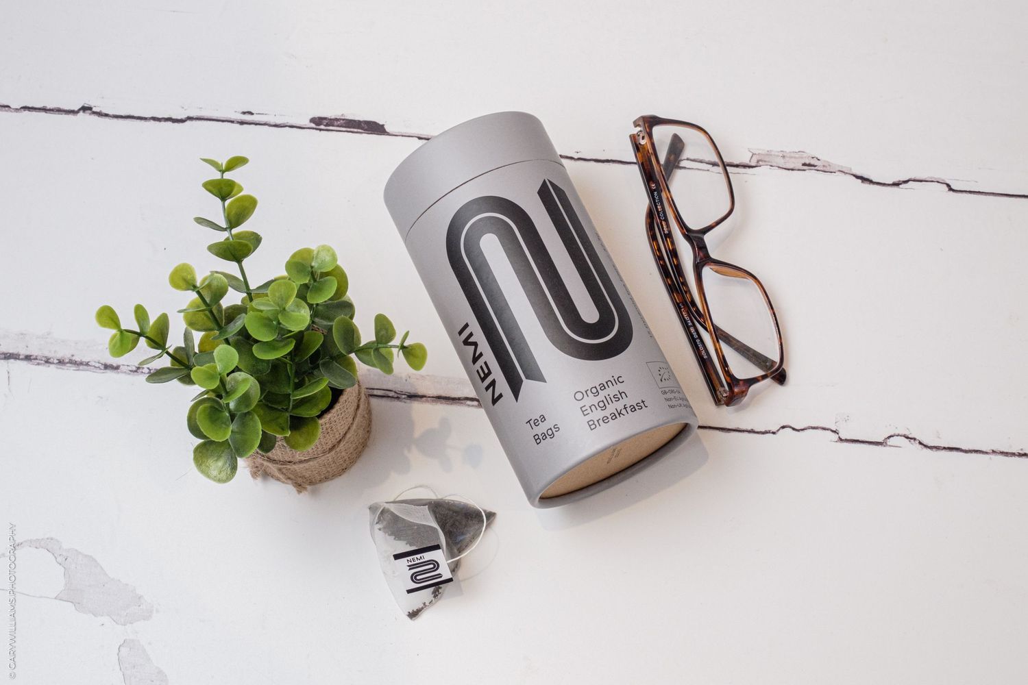 Gray reusable water bottle on marble surface with reading glasses and small potted succulent plant.