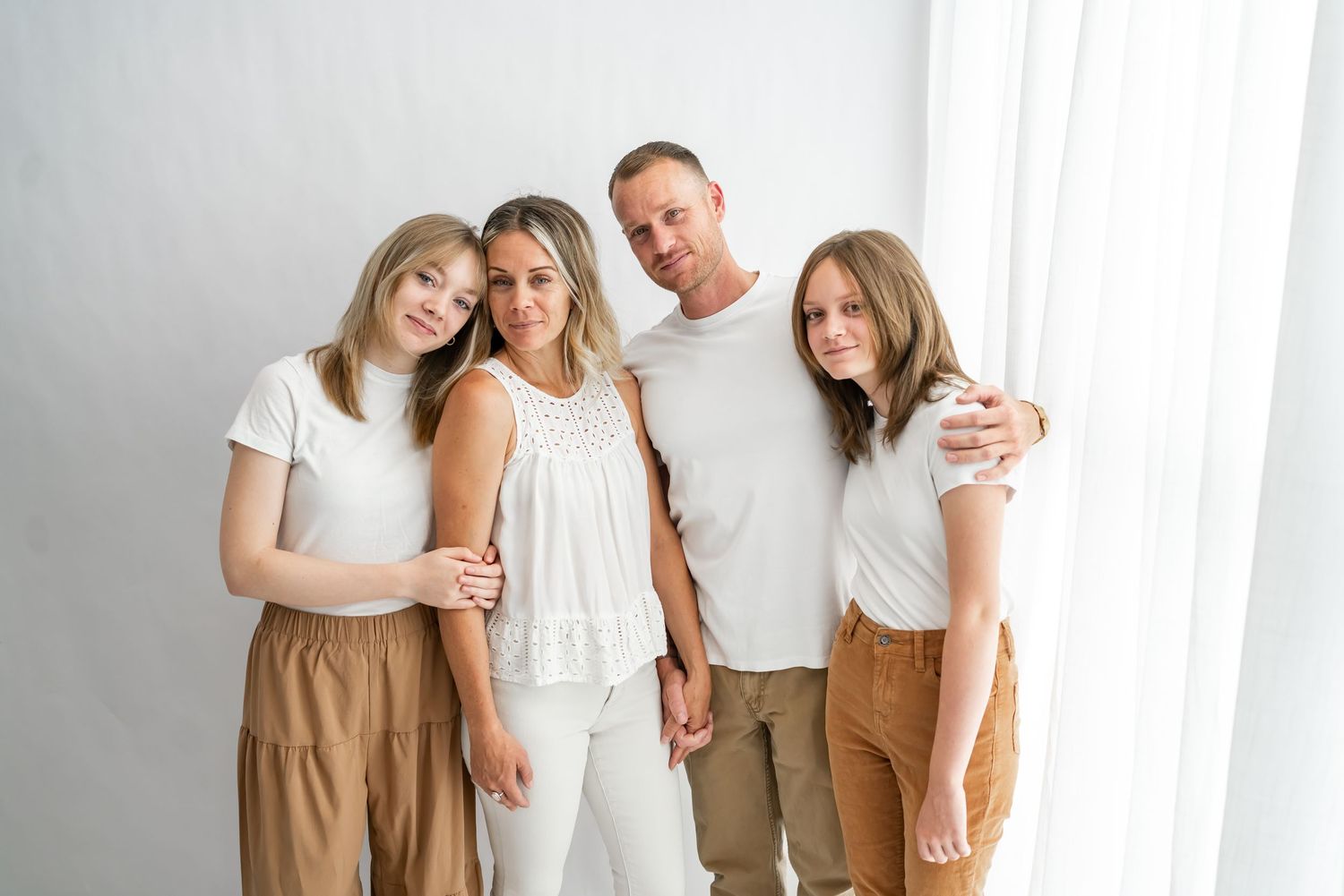 Family members in coordinating white and tan outfits pose together for casual studio portraits.