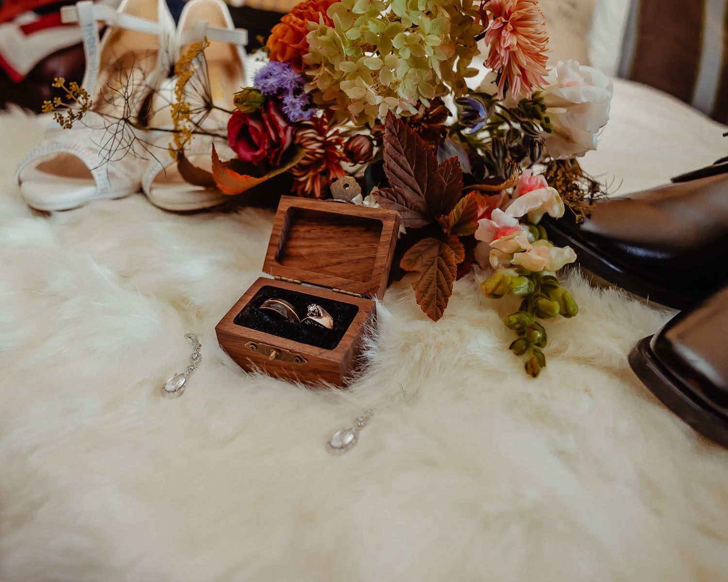 Wedding detail shot of wooden ring box with floral arrangements and bridal accessories.