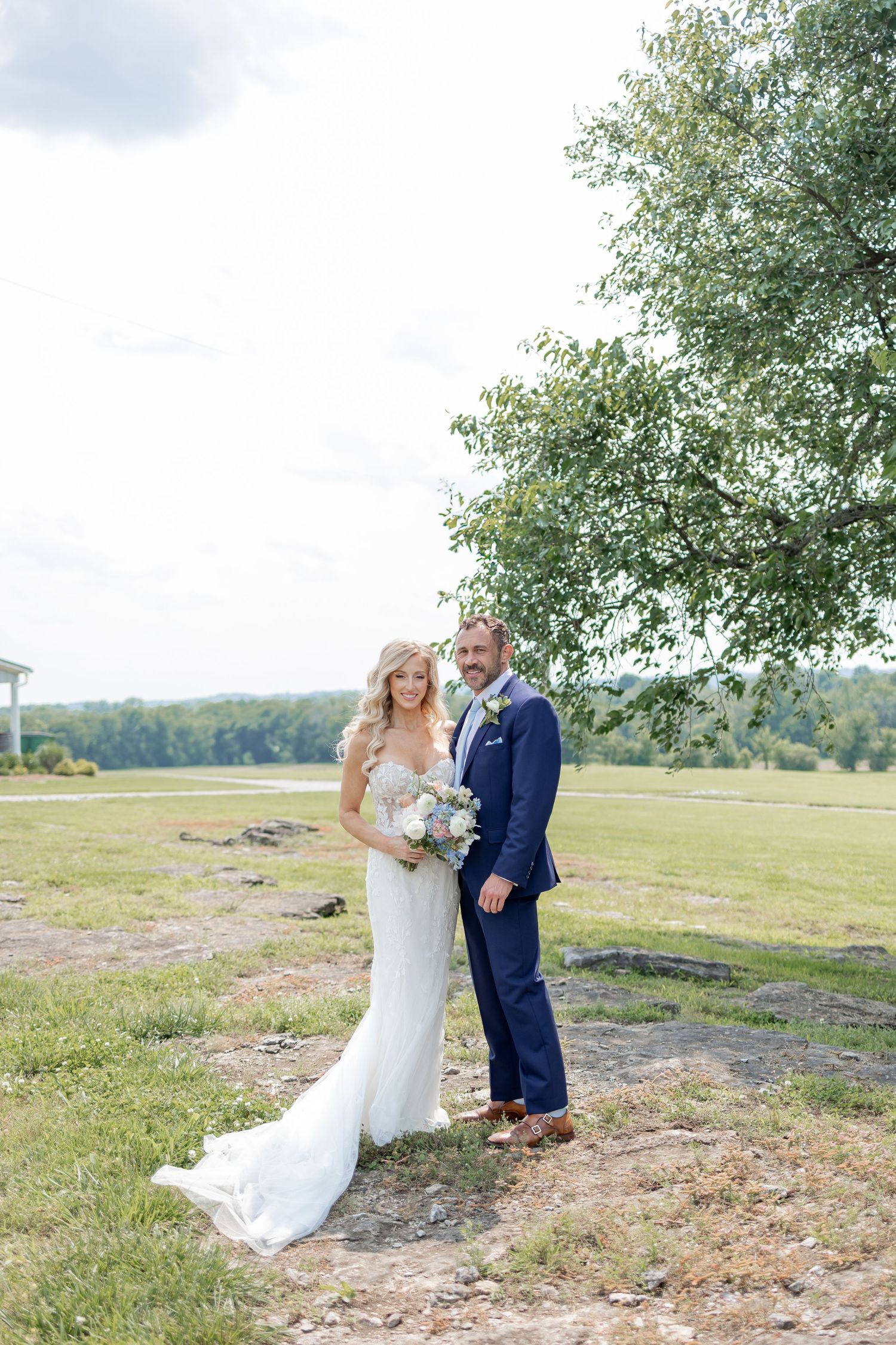 A couple in wedding attire shares an intimate moment together in a scenic outdoor field setting.