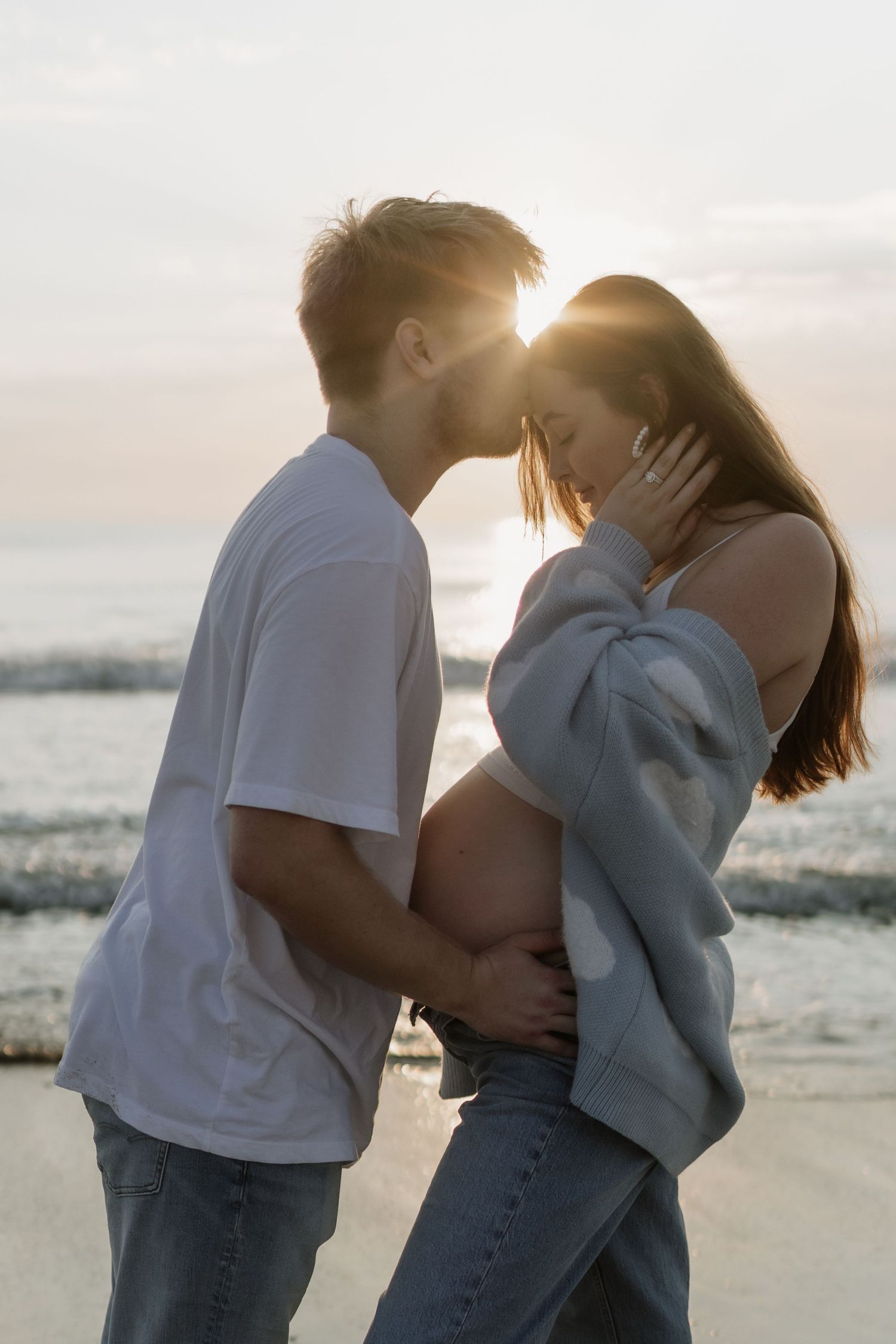 Couple embracing on beach at sunset with ocean waves in background.